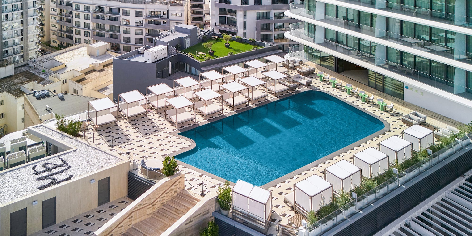 Modern hotel rooftop pool with white cabanas and urban cityscape.