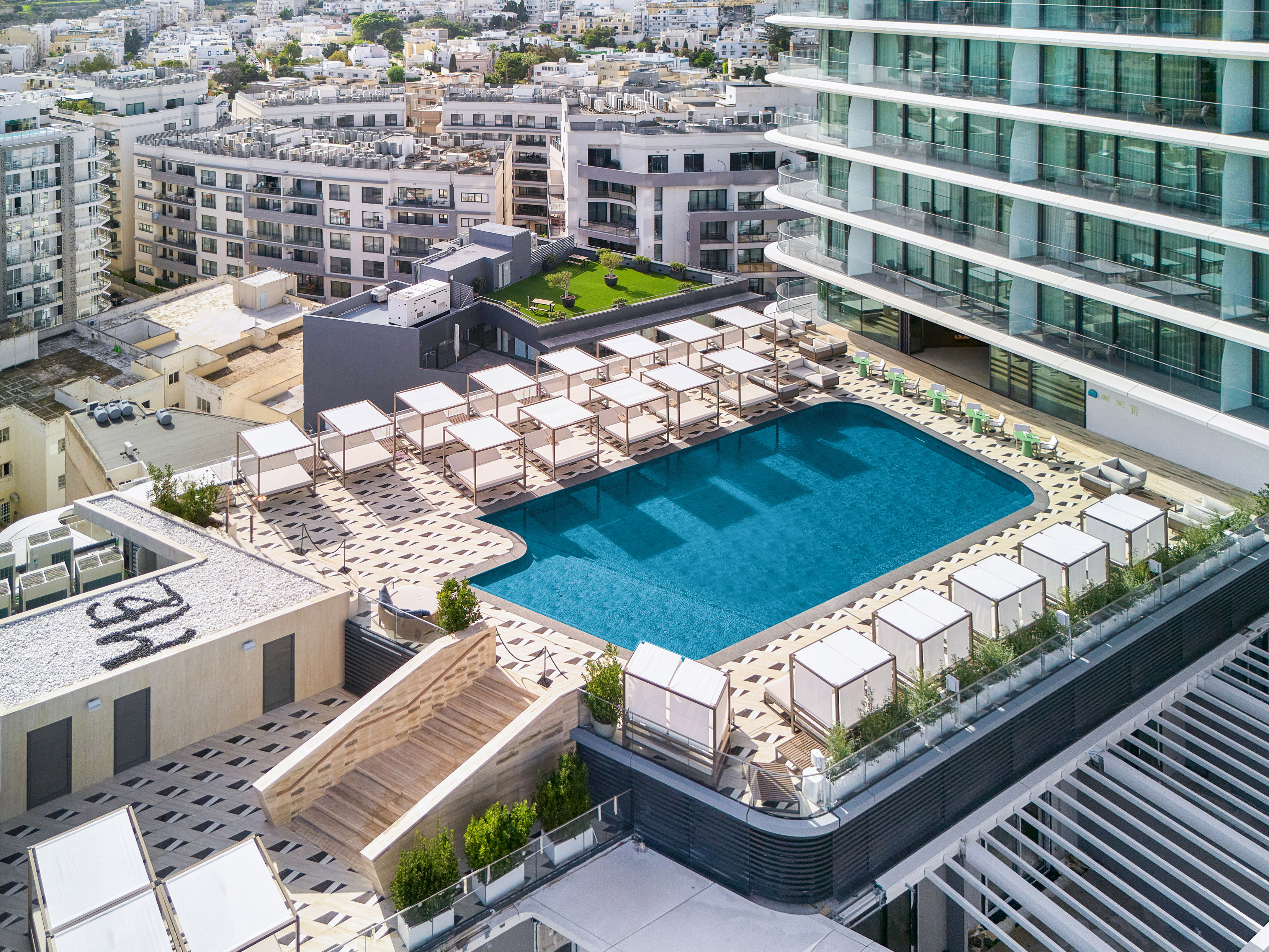 Modern hotel rooftop pool with cabanas, lounge seating, and city view.