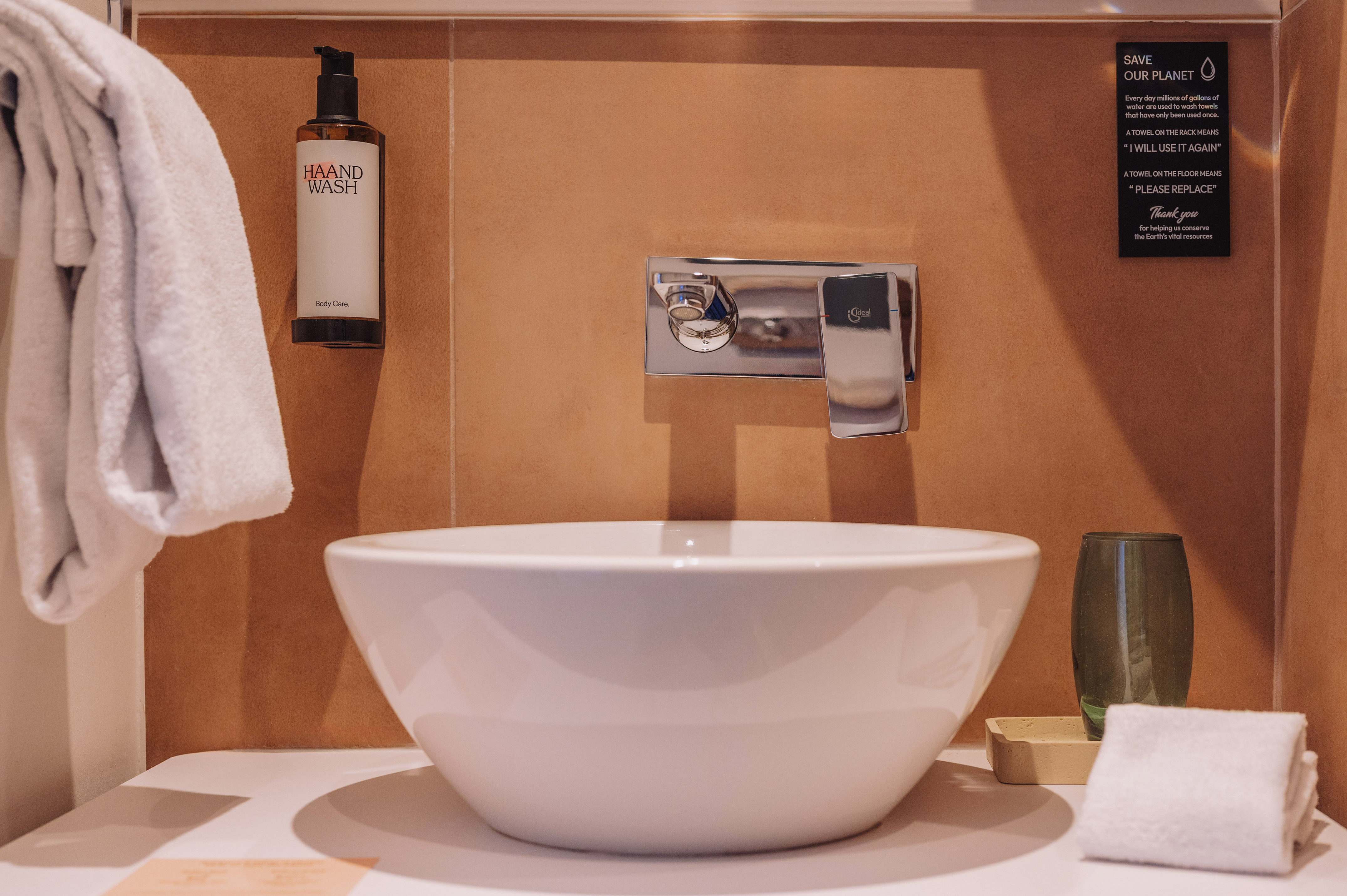 Hotel bathroom sink with HAAND WASH soap, chrome faucet, and eco-friendly sign.