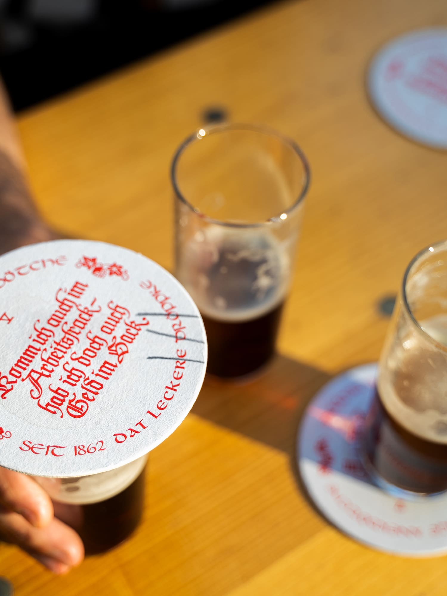 Two glasses of dark beer with Uerige branded coasters on a sunny wooden table.