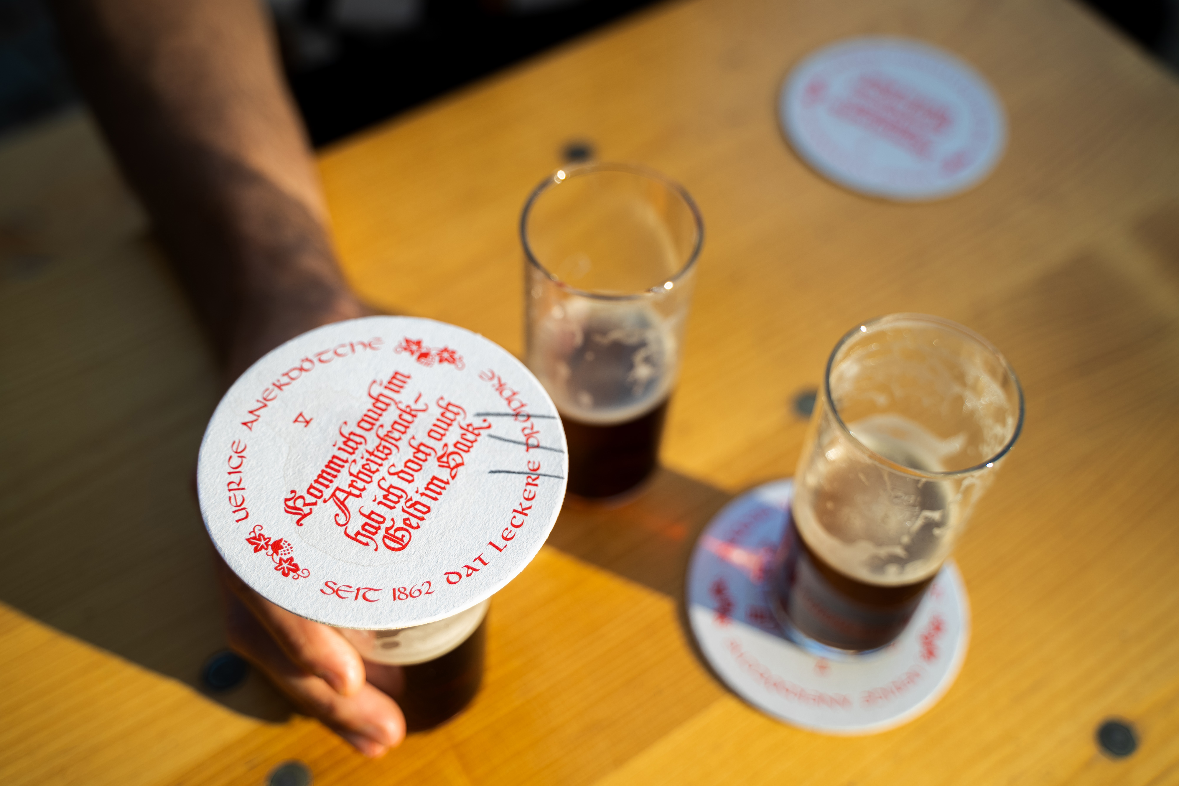 Two glasses of dark beer with Uerige branded coasters on a sunny wooden table.