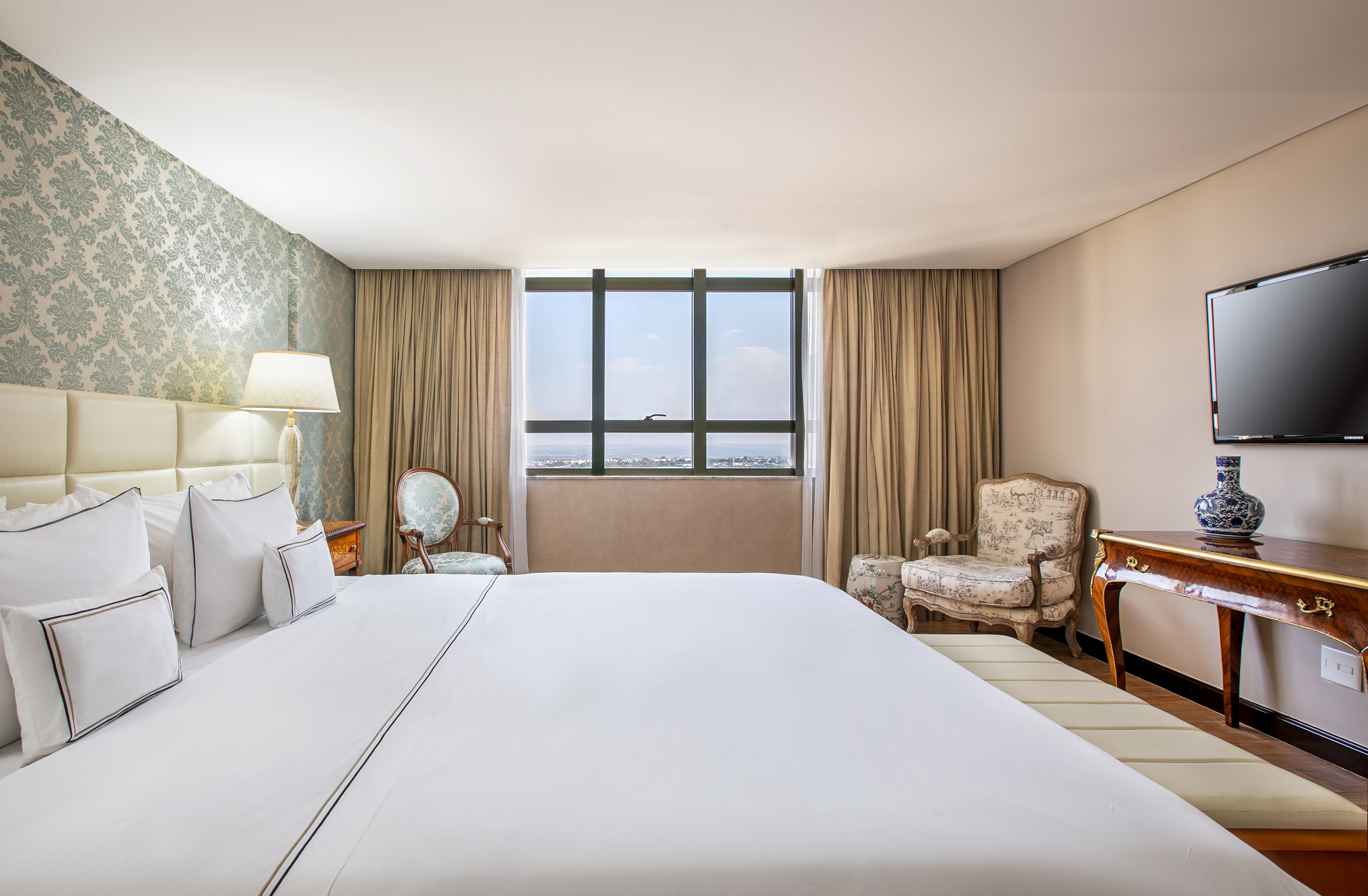 Elegant hotel room with large bed, patterned wallpaper, and city view.