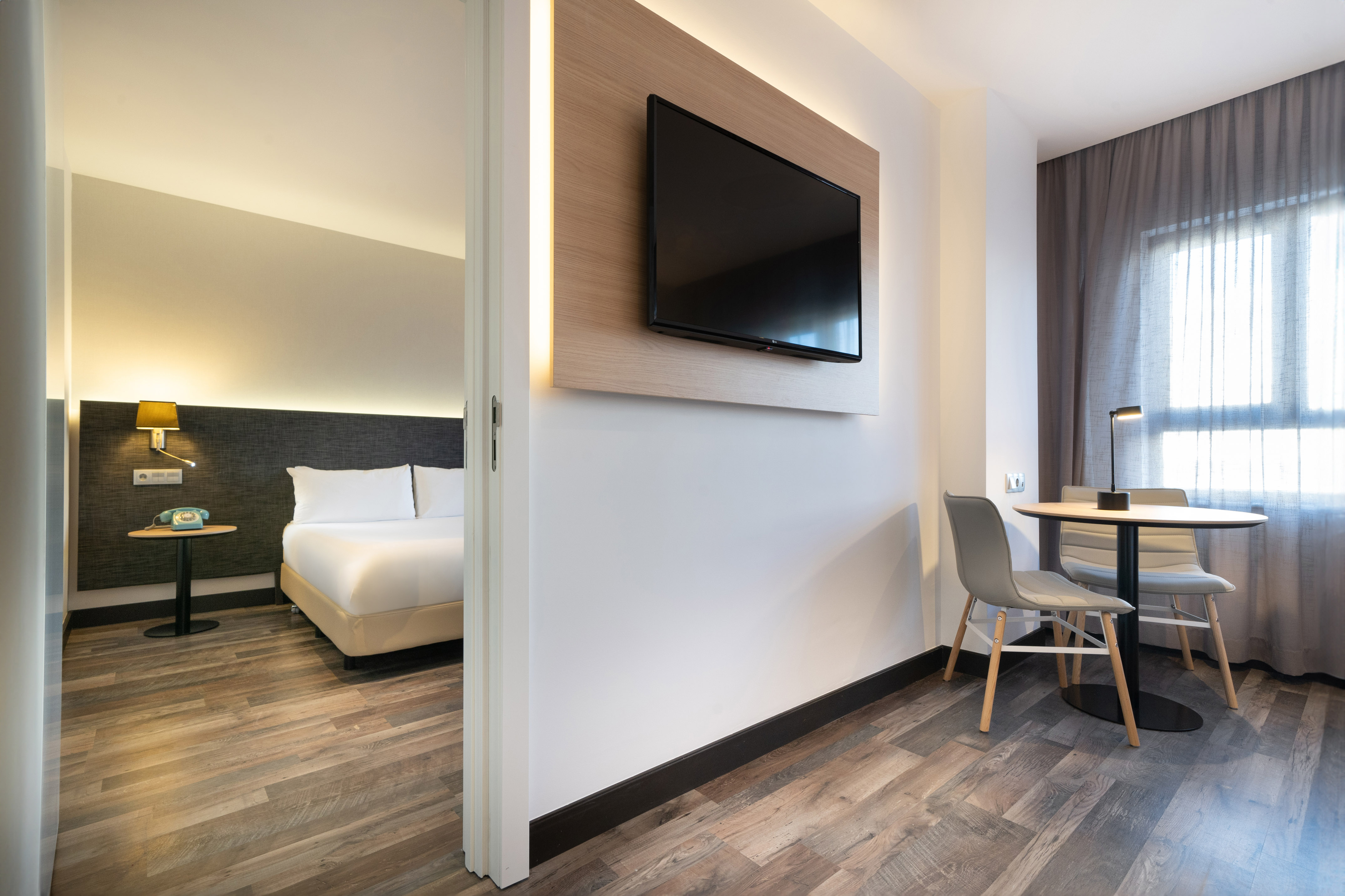 Sleek hotel room featuring a bedroom, smart TV, and dining nook with chairs.