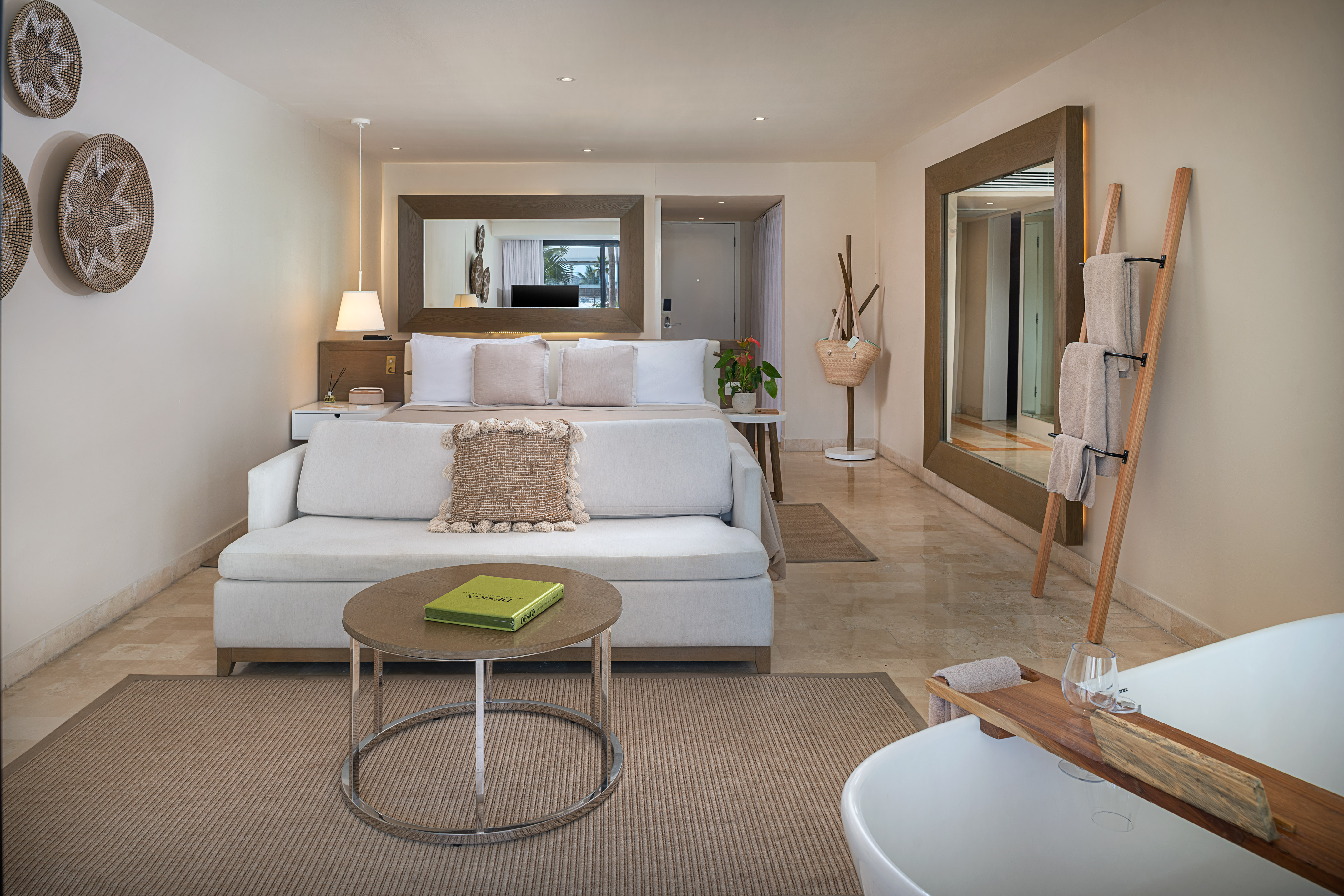 Modern hotel suite with bed, sofa, large mirrors, and freestanding tub.