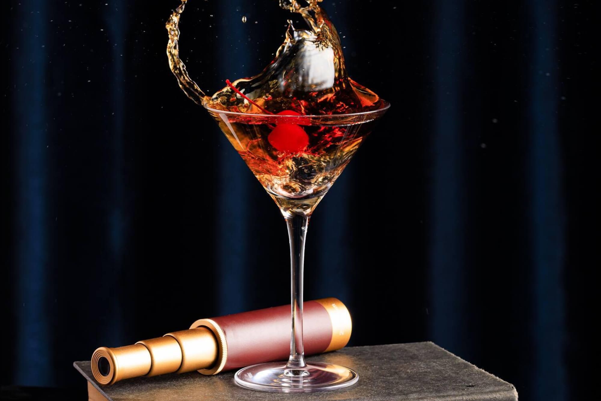Martini cocktail splash with cherry, on vintage book and brass spyglass.