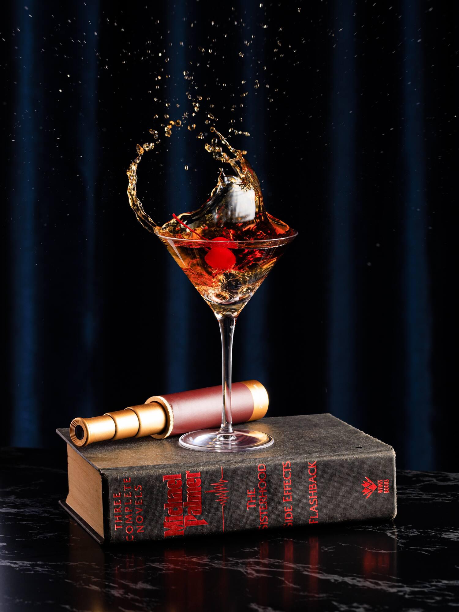 Martini cocktail splash with cherry, on vintage book and brass spyglass.