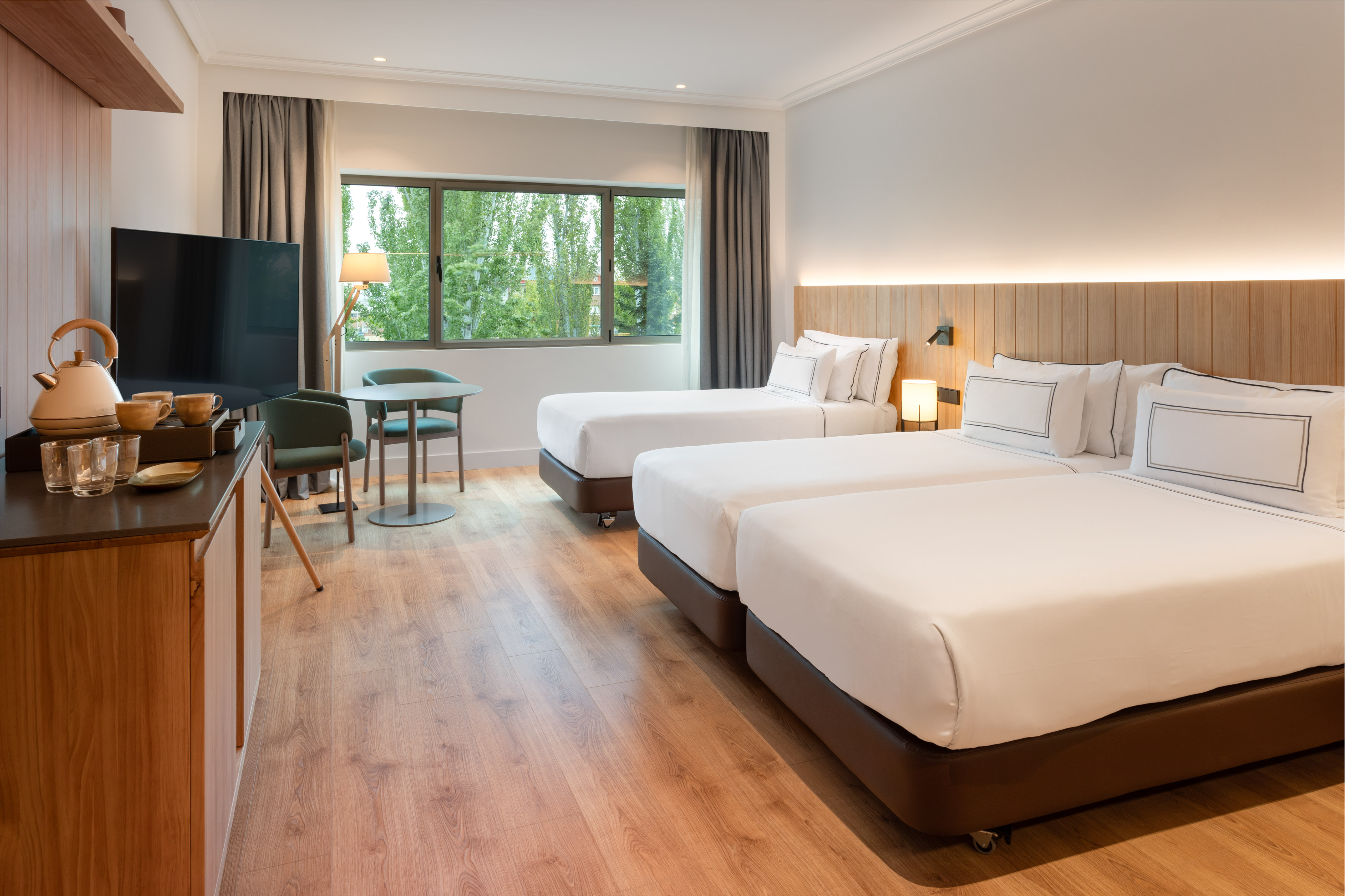 Modern hotel room with twin beds, bright window, and wooden floor.