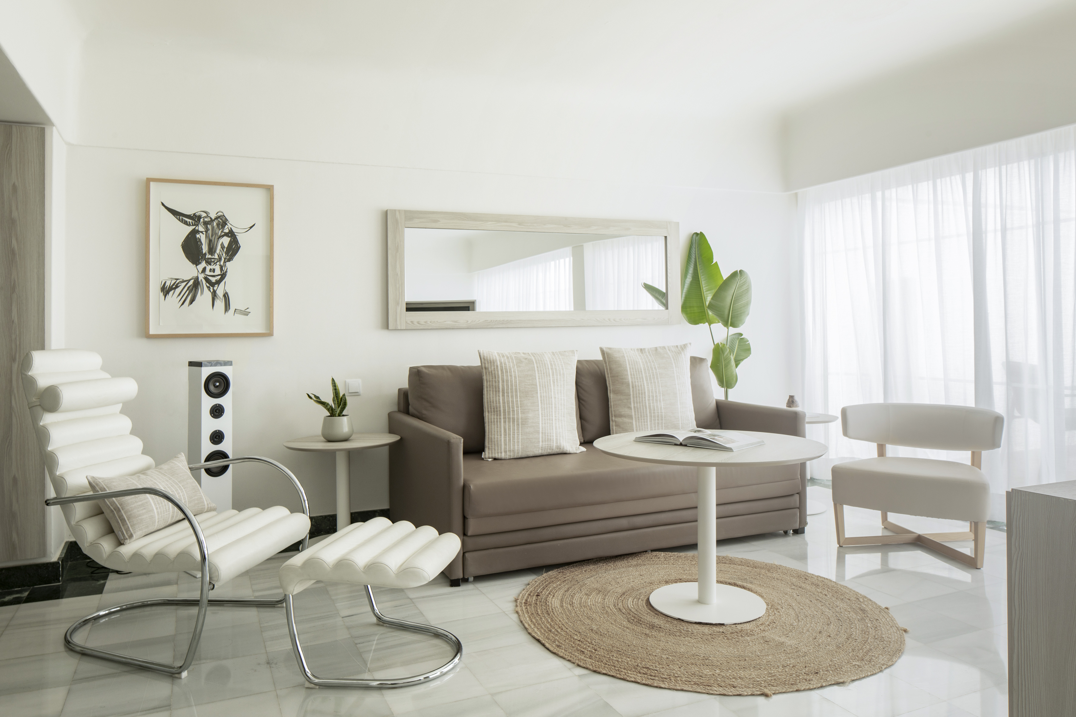 Modern living room: taupe sofa, white chairs, framed goat art, and large mirror.