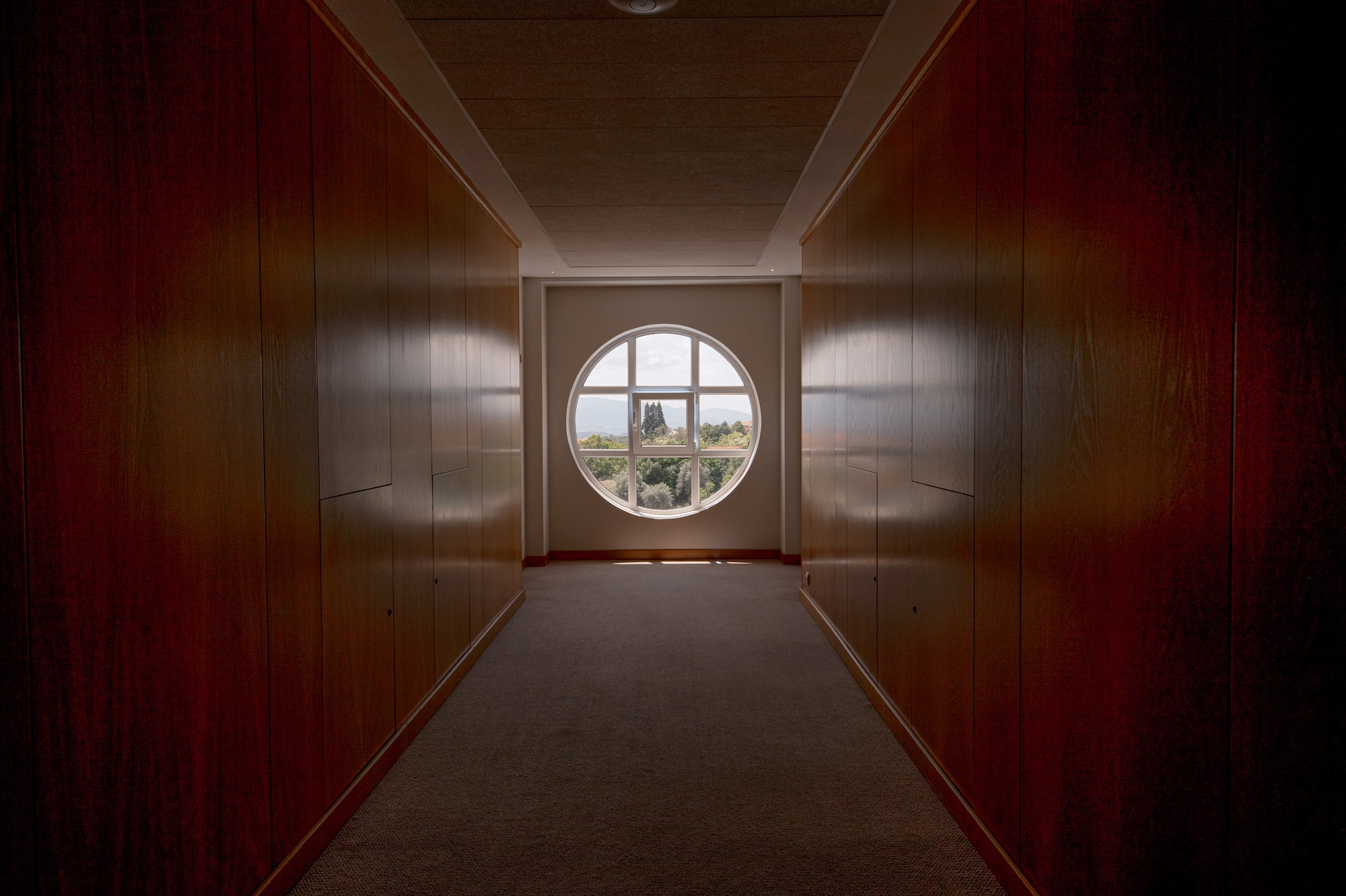 Modern interior hallway with dark wood panels and round window view.