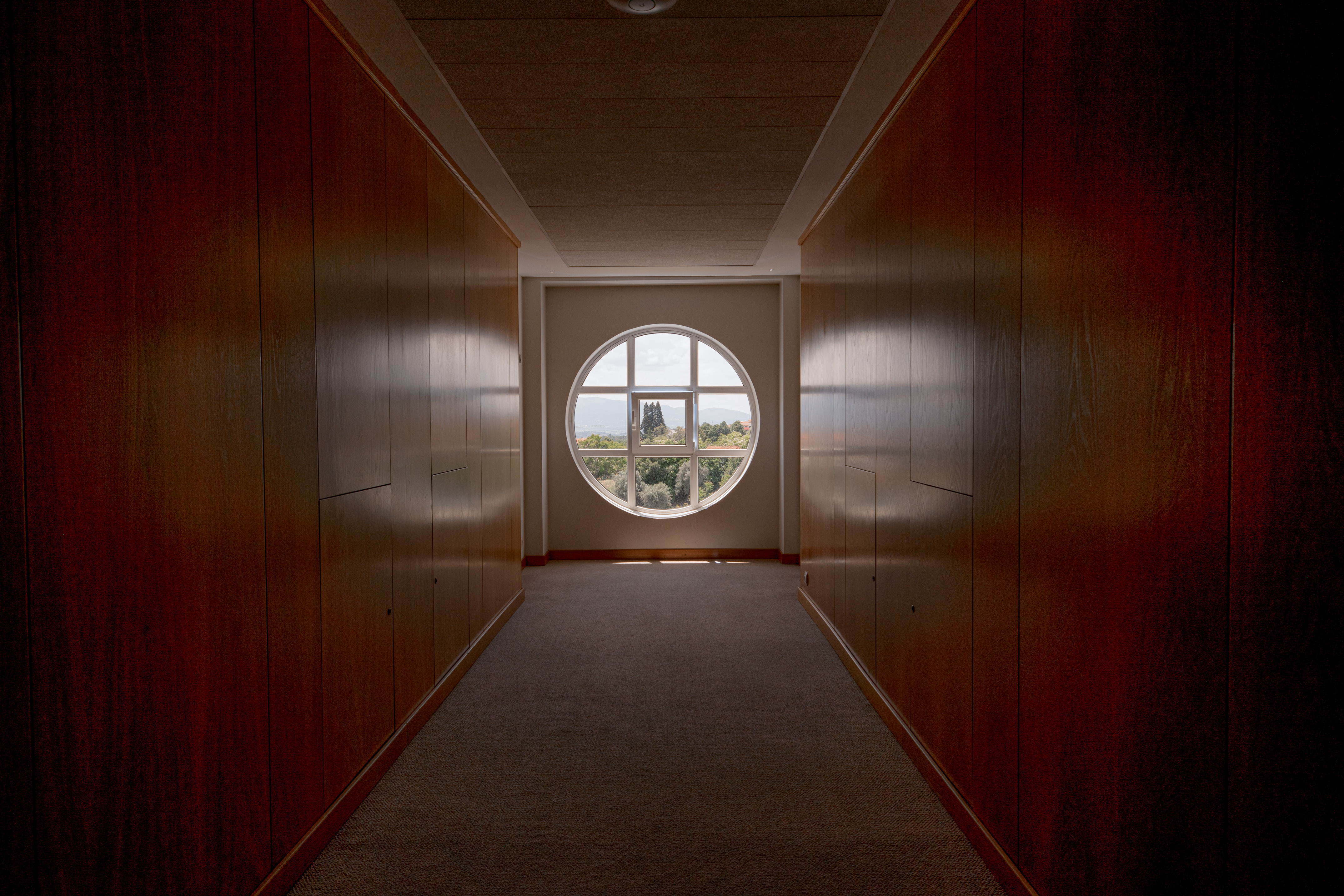 Modern interior hallway with dark wood panels and round window view.