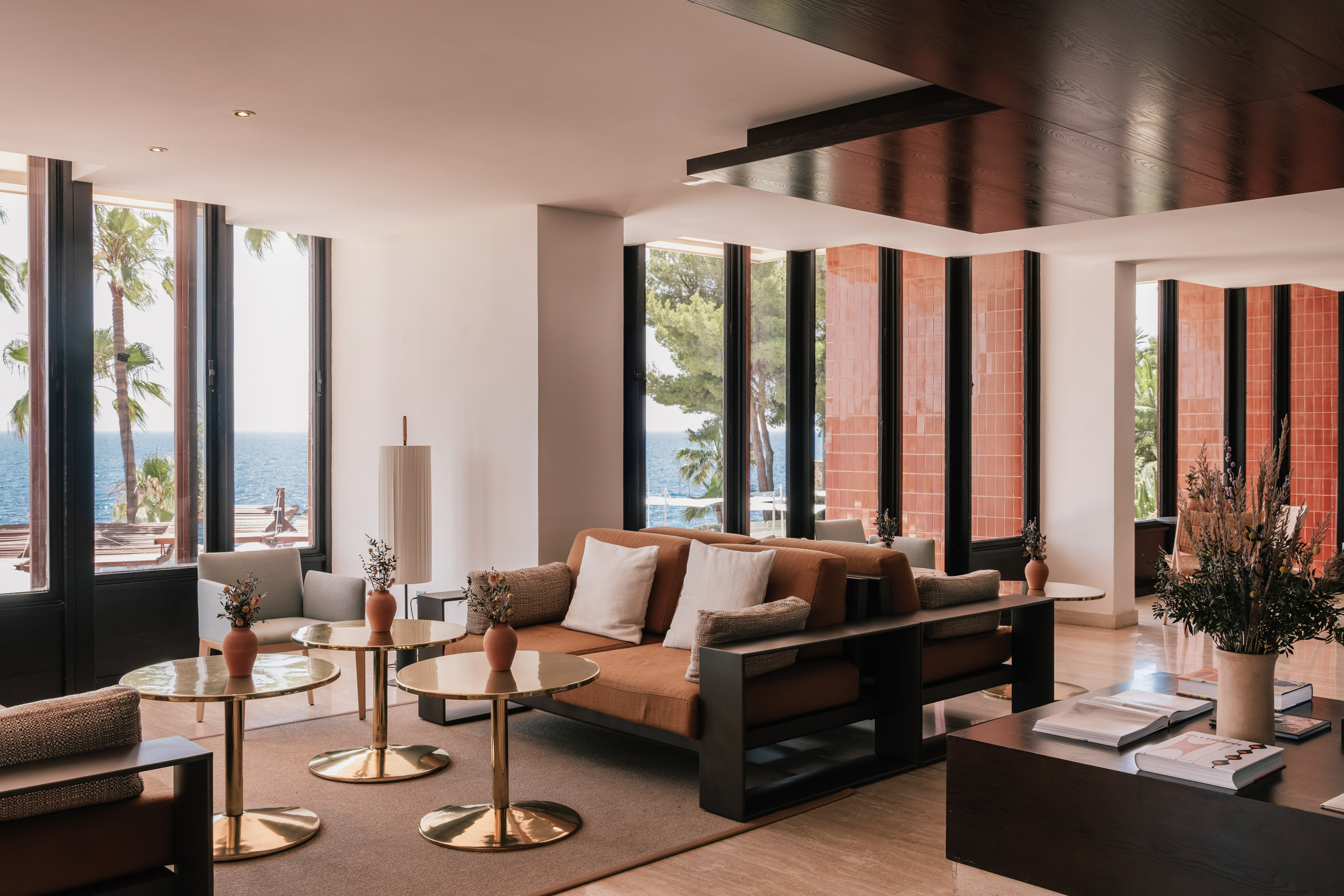 Modern hotel lounge overlooking the sea with rust sofas and brass tables.