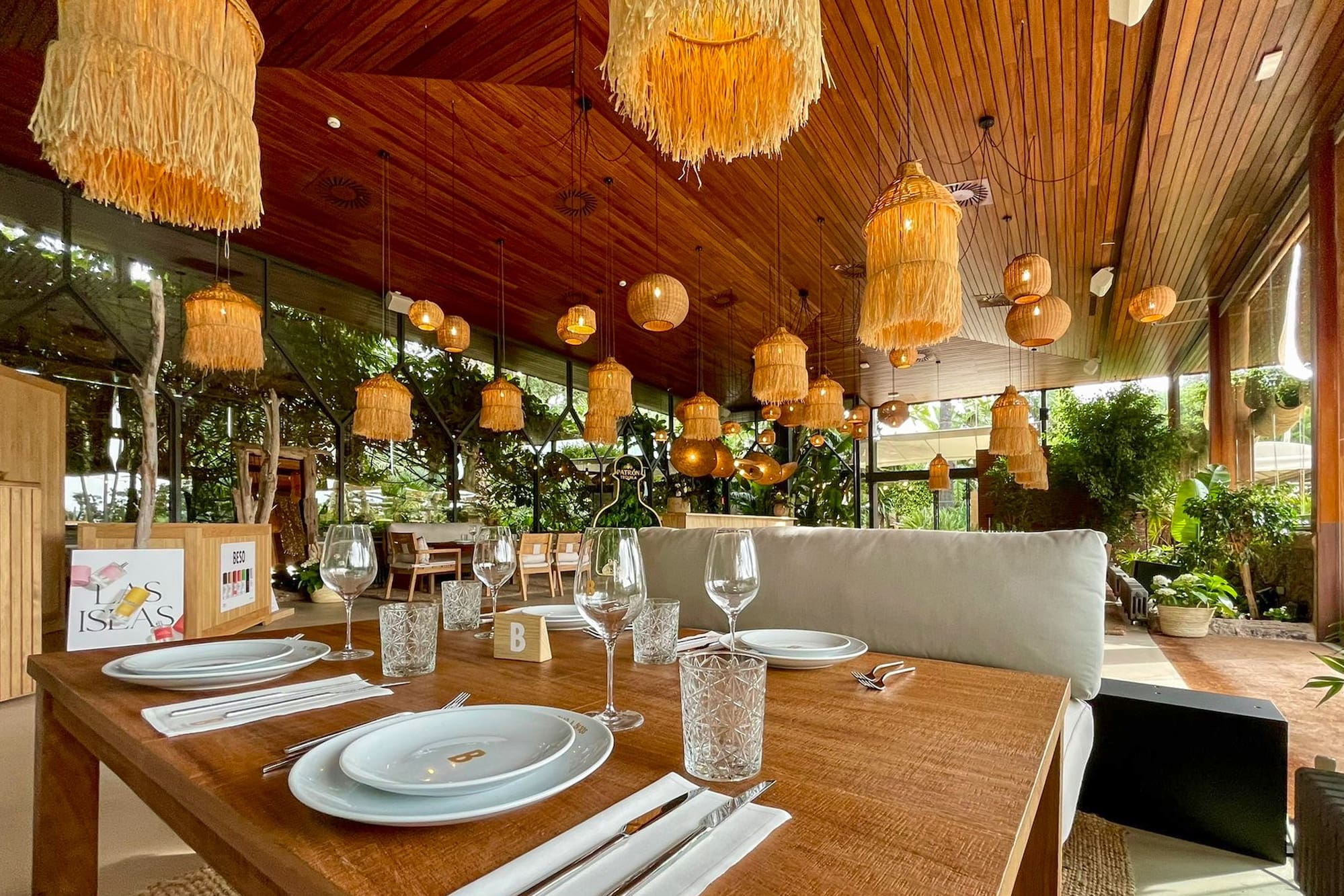 Tropical restaurant dining with rattan lights, wooden ceiling, and lush plants.