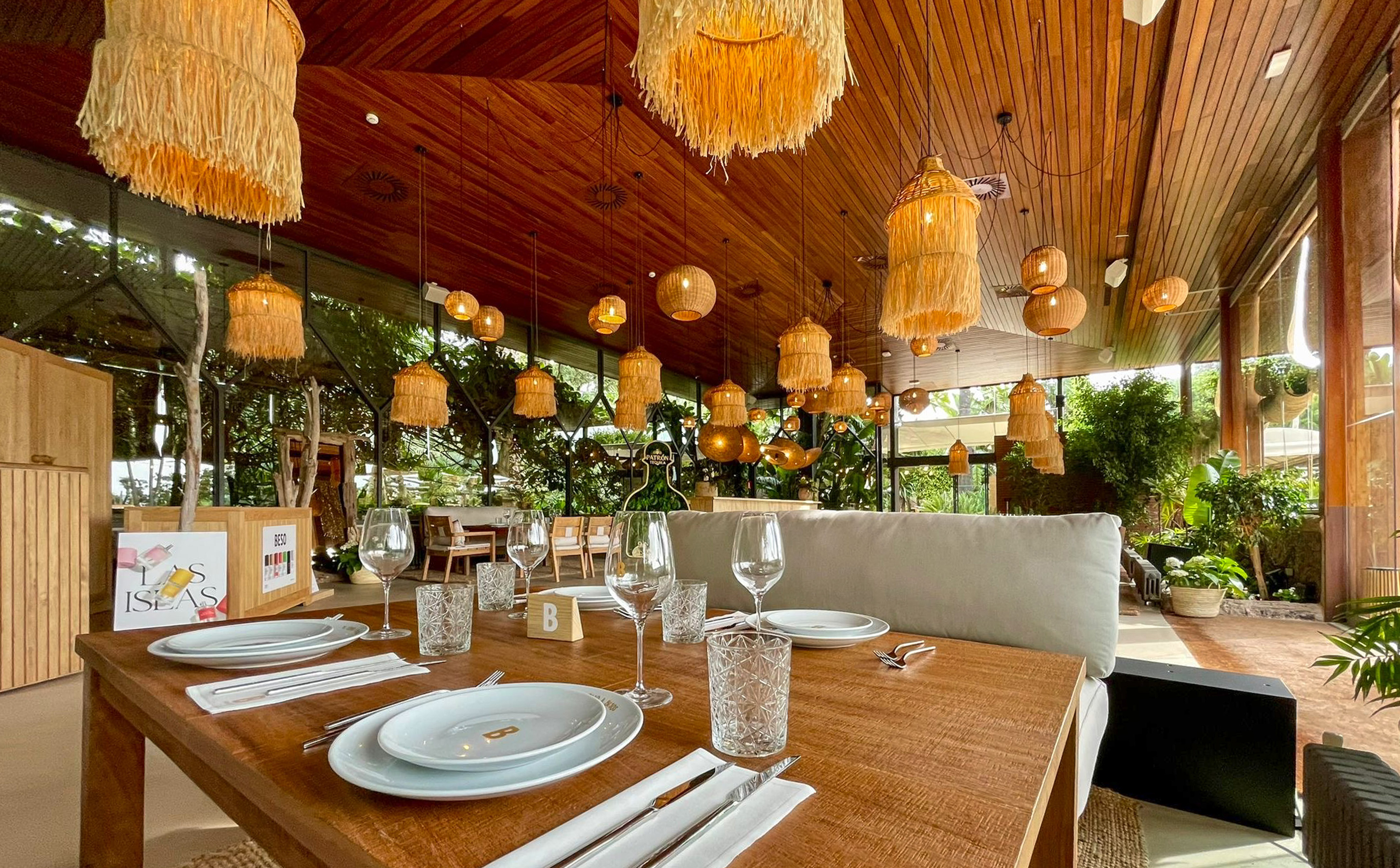 Tropical restaurant dining with rattan lights, wooden ceiling, and lush plants.