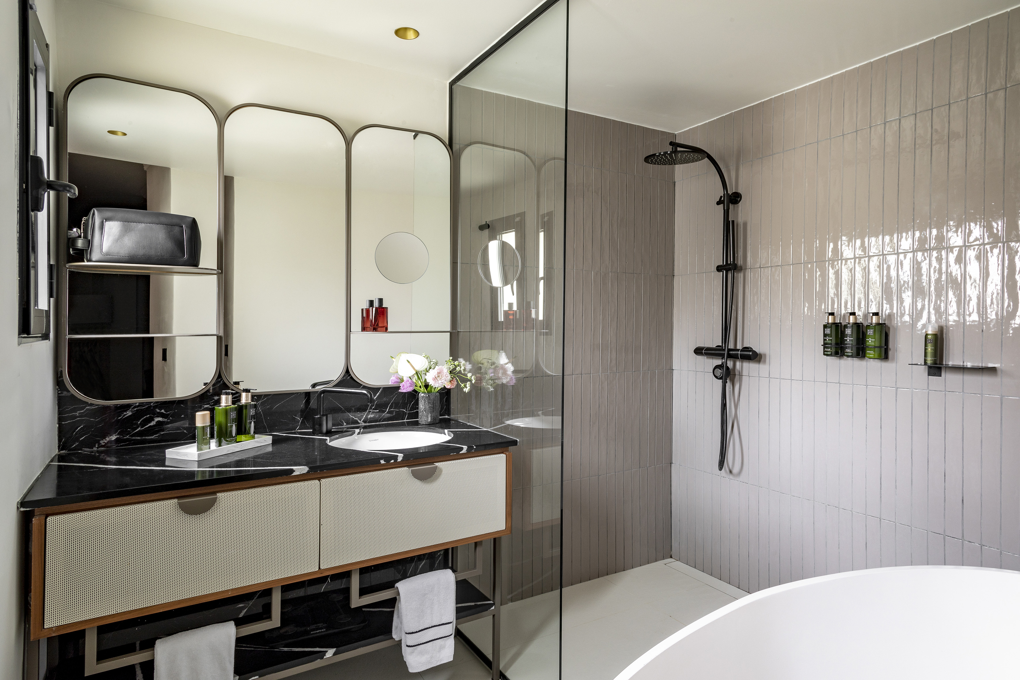 Modern hotel bathroom: black marble vanity, arched mirrors, glass shower.