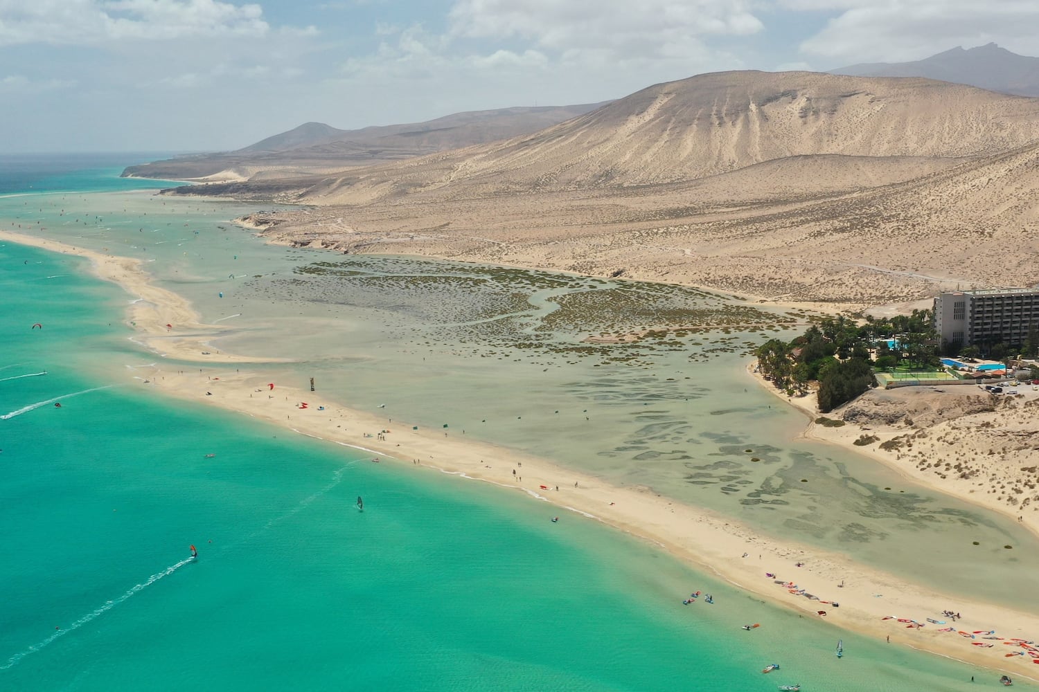 Turquoise ocean, lagoon, kitesurfers, Fuerteventura beach, arid mountains.
