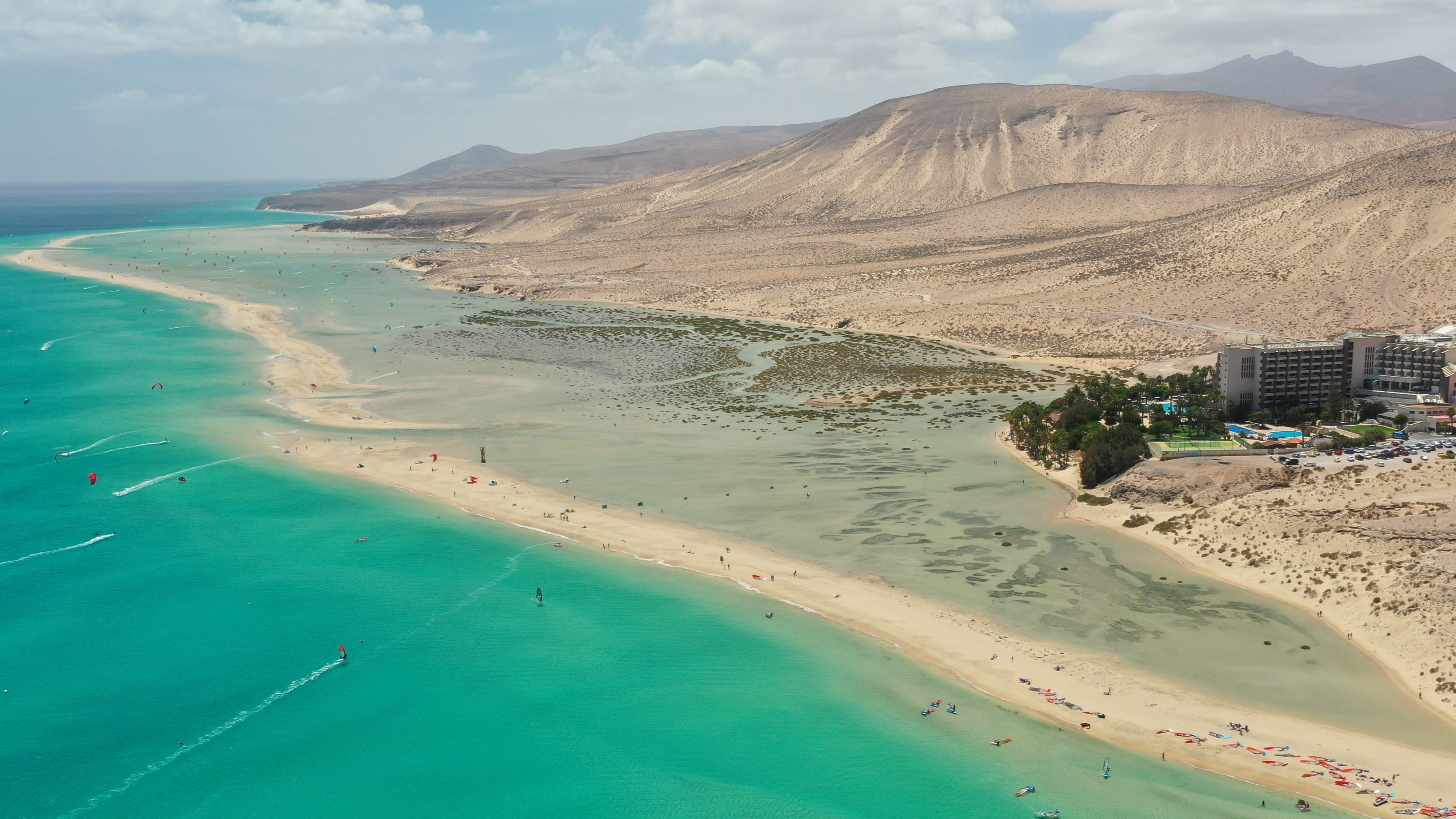 Turquoise ocean, lagoon, kitesurfers, Fuerteventura beach, arid mountains.