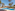 Tropical resort pool with palm trees, sun loungers, and colorful buildings.