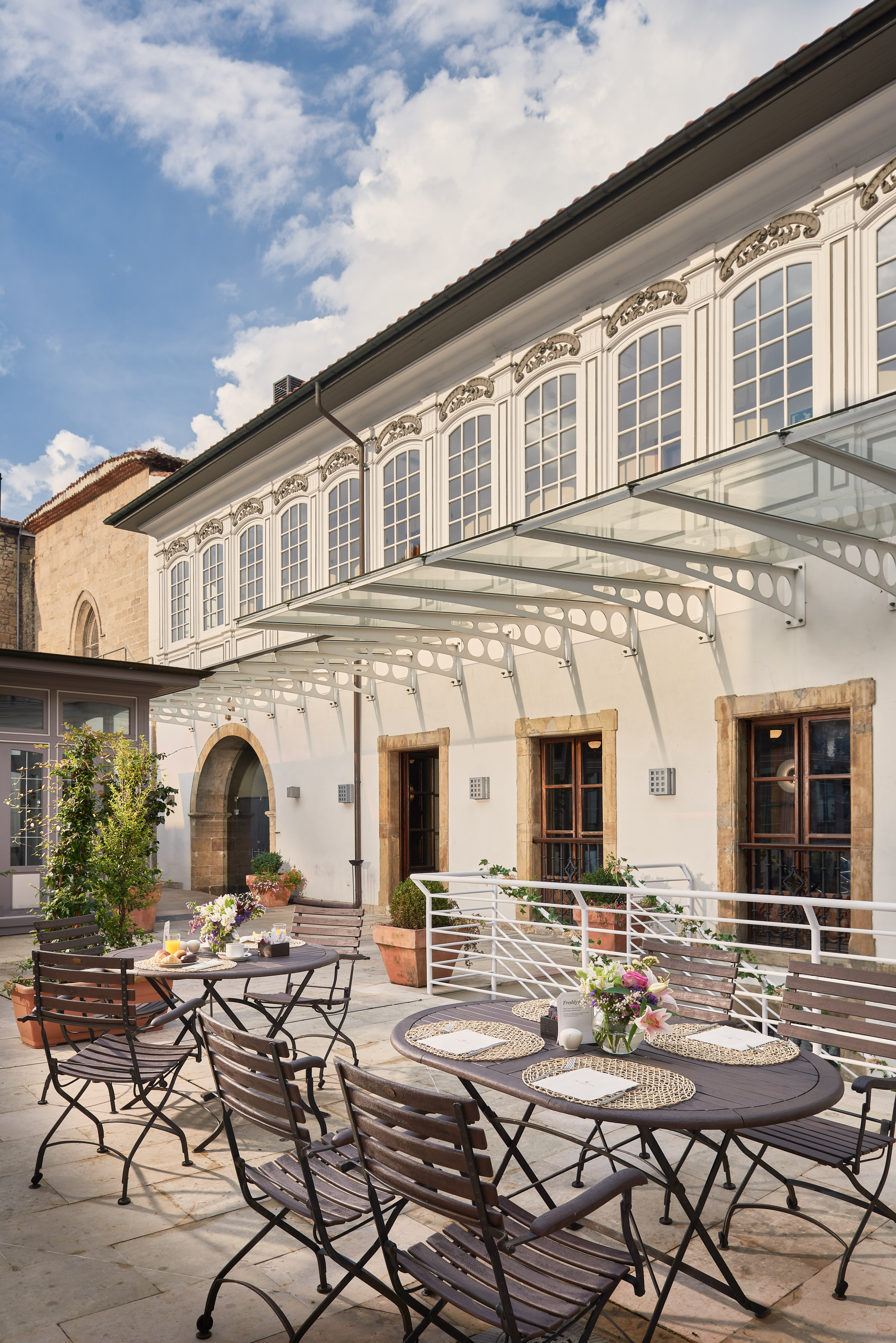 Sunny outdoor breakfast patio with tables, glass awning, and ornate facade. - Buffet Espolita, Cuisine internationale - Palacio de Avilés Affiliated by Meliá, Avilés