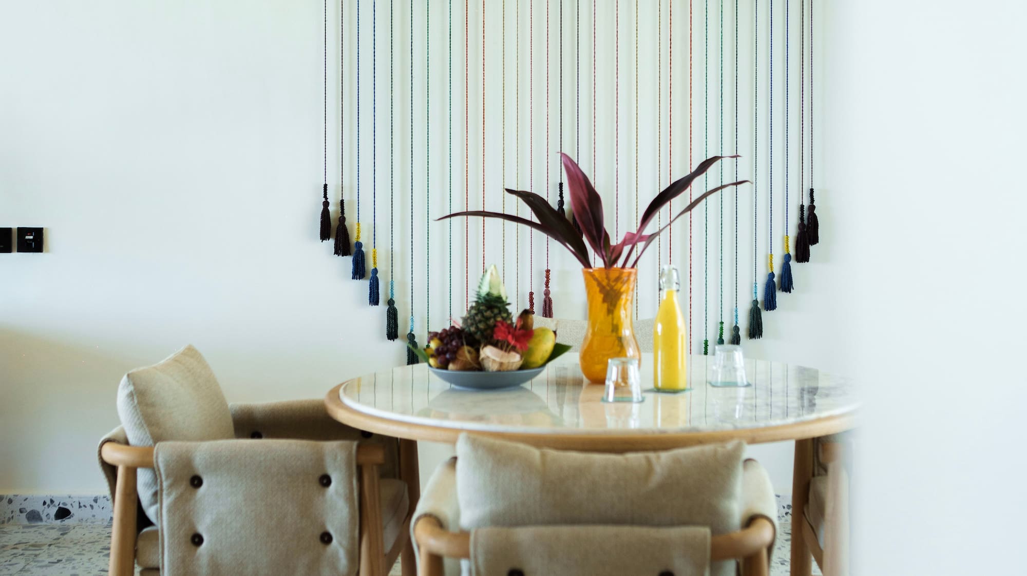 Modern dining room with wood table, fruit, colorful wall art, and woven ceiling.