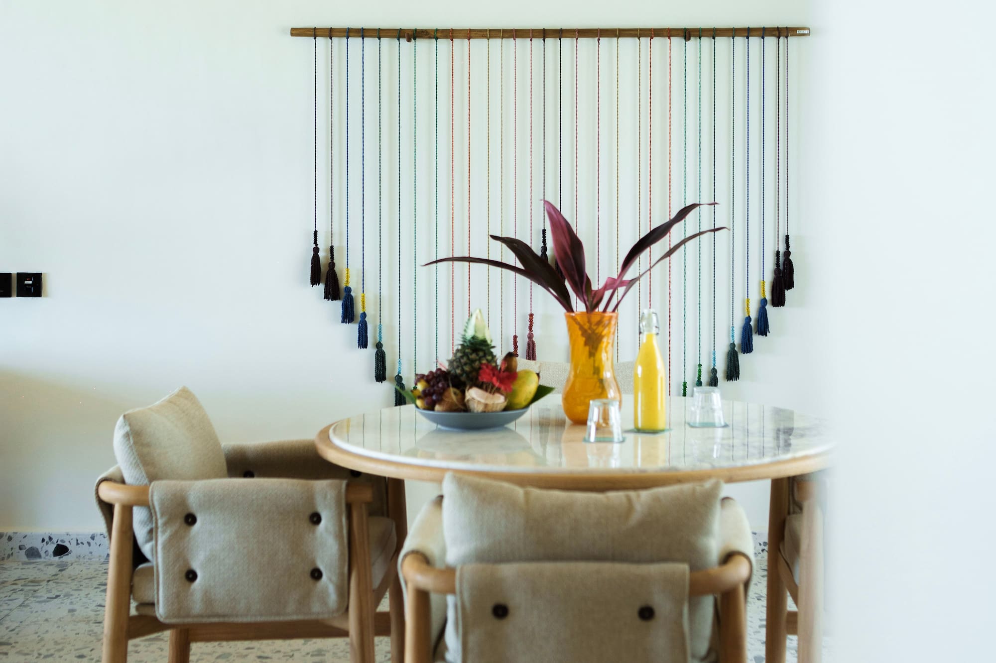 Modern dining room with wood table, fruit, colorful wall art, and woven ceiling.
