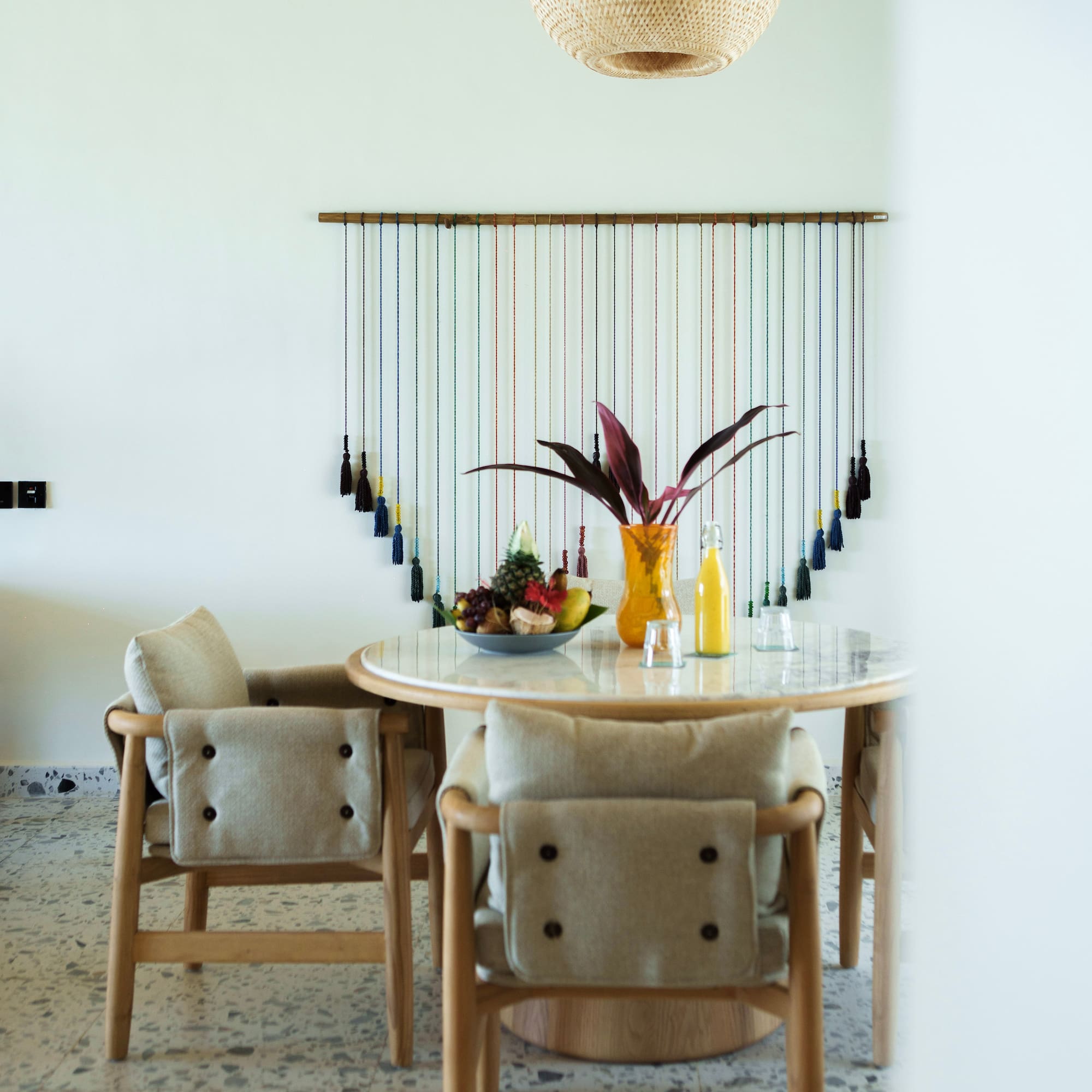 Modern dining room with wood table, fruit, colorful wall art, and woven ceiling.