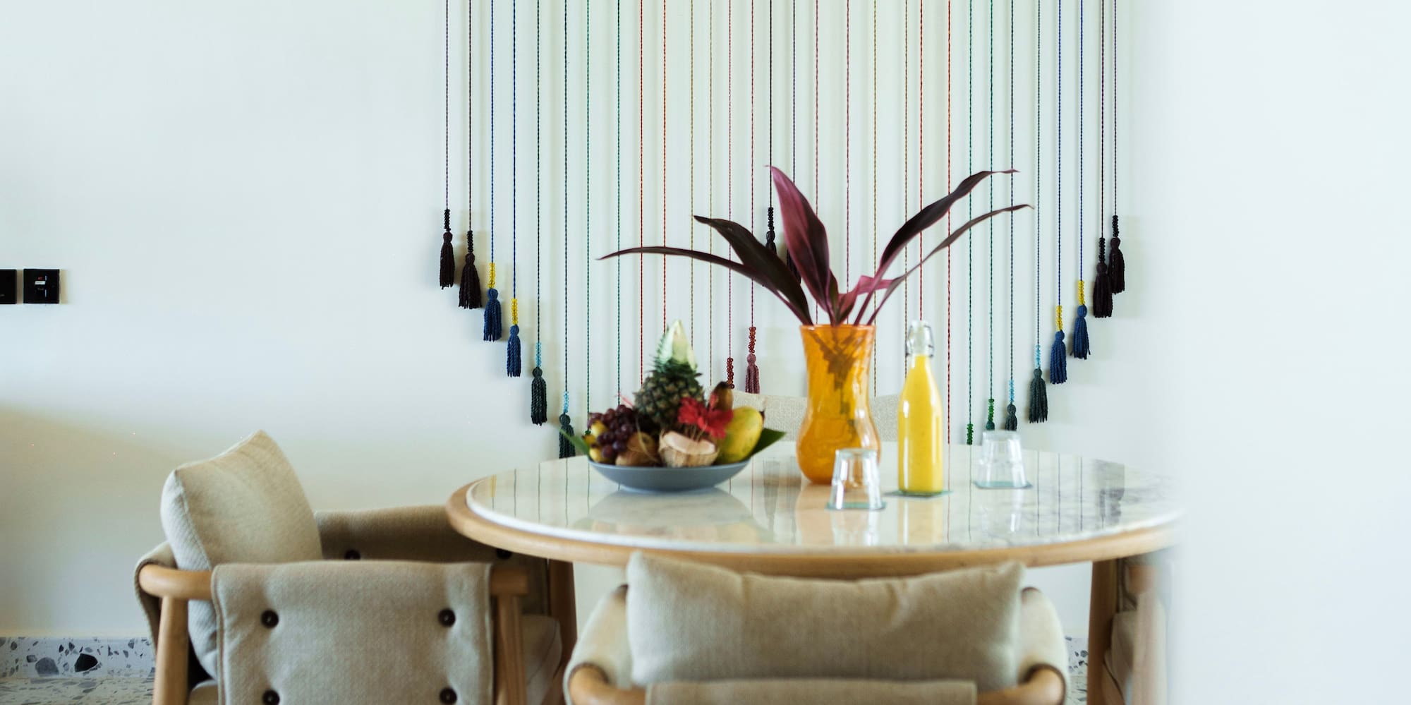 Modern dining room with wood table, fruit, colorful wall art, and woven ceiling.