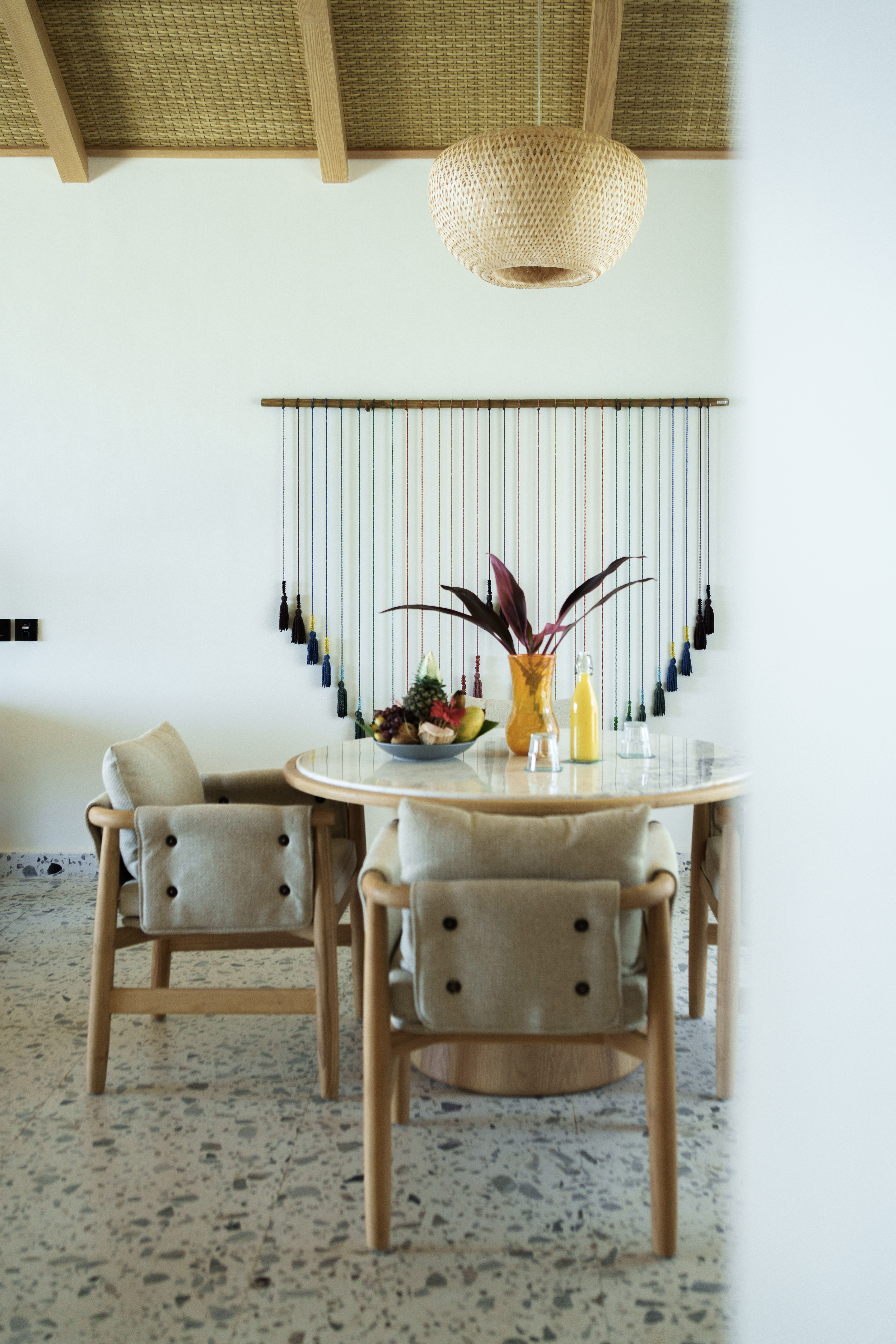 Modern dining room with wood table, fruit, colorful wall art, and woven ceiling.