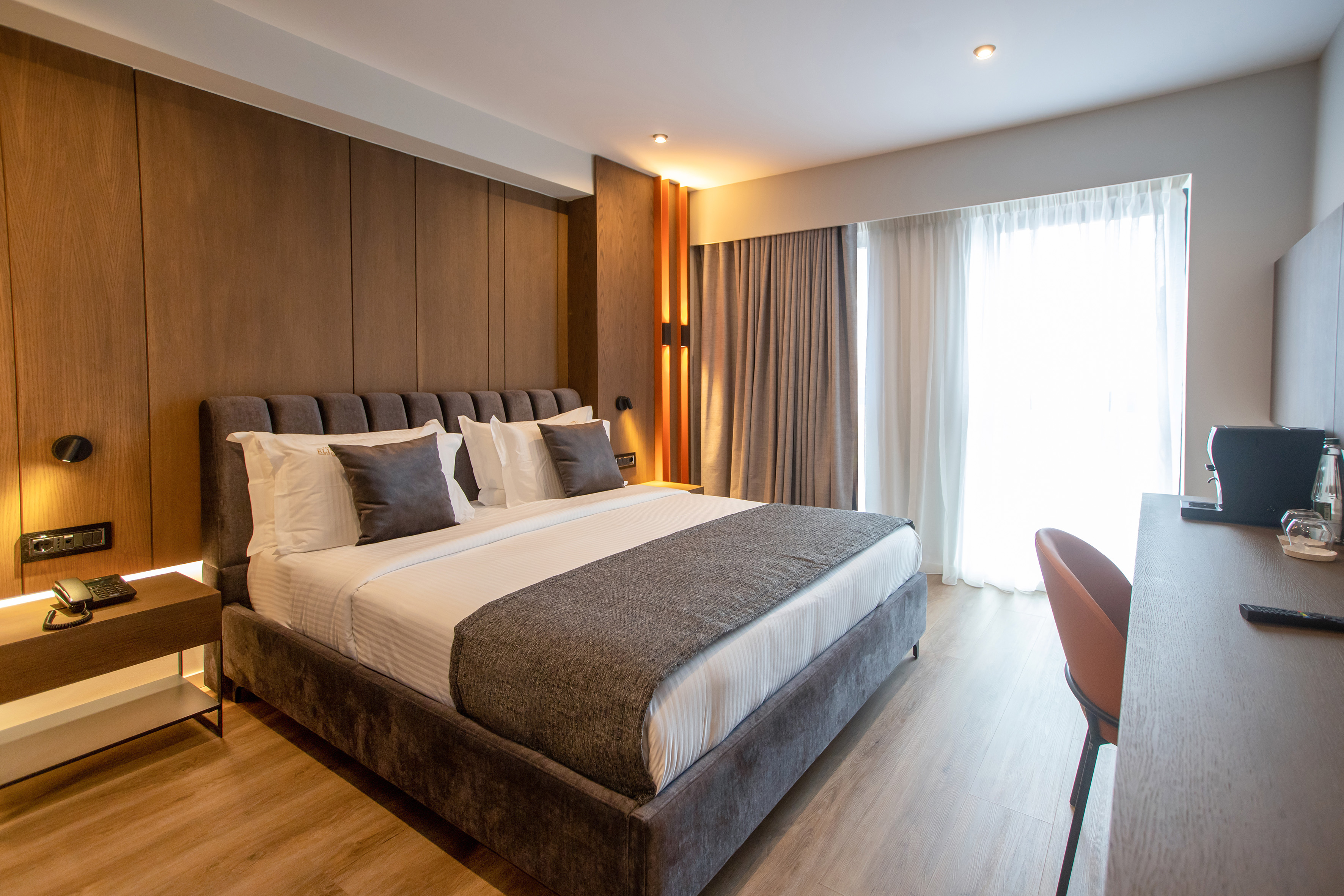 Modern hotel bedroom with king bed, wood paneling, and warm lighting.