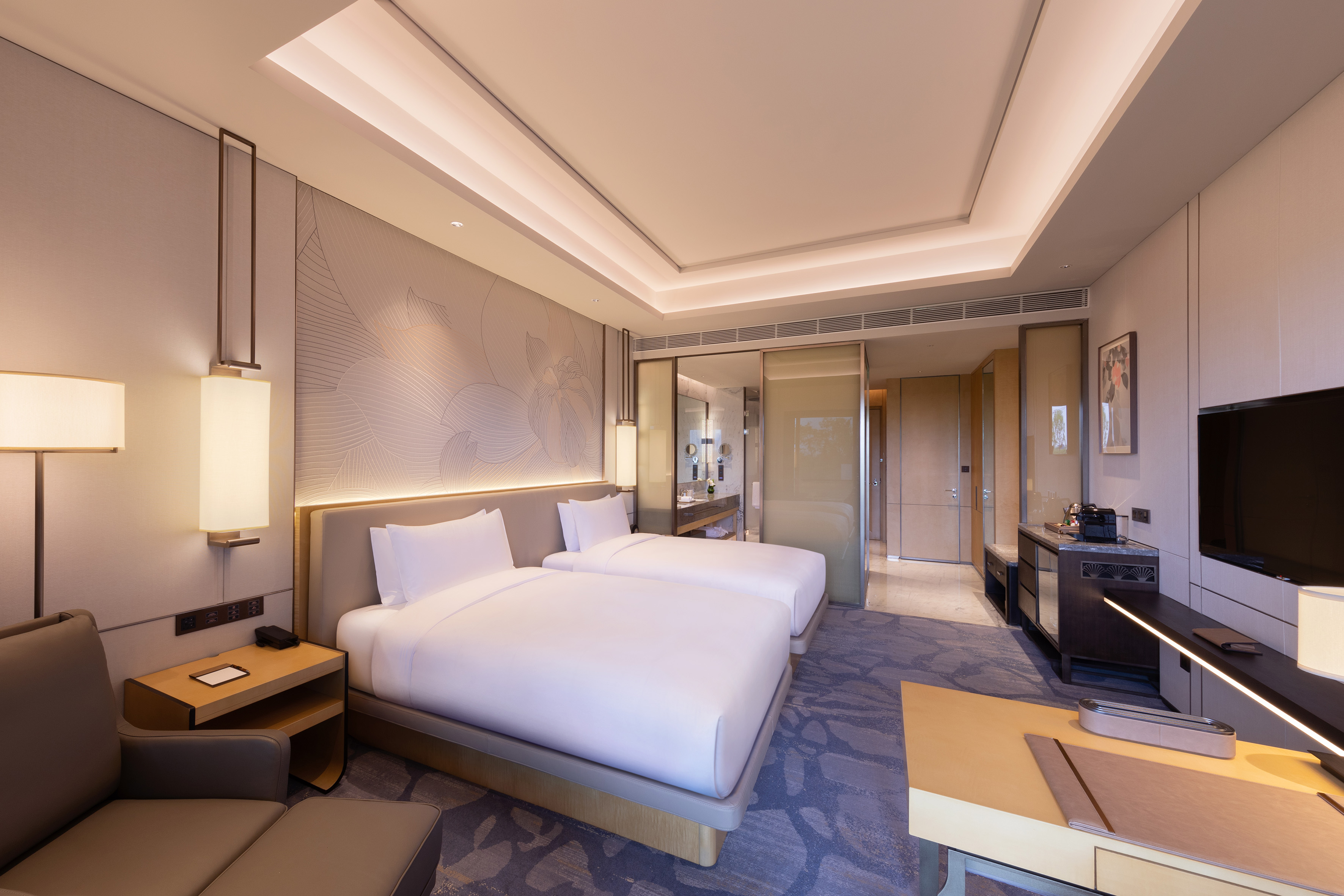 Modern hotel room with twin beds, warm lighting, and luxury decor.
