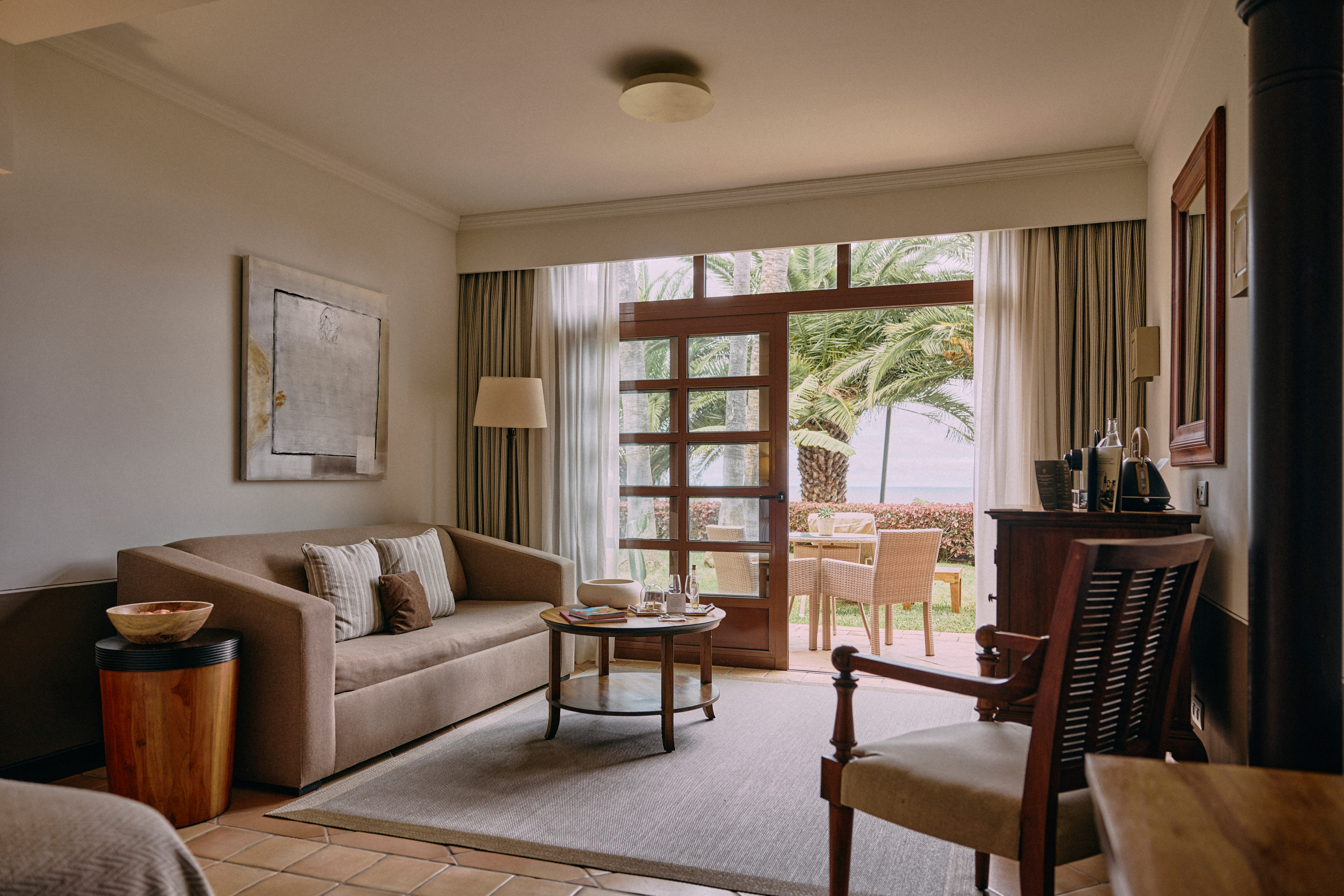 Hotel living room with sofa, coffee table, patio door, and tropical palm tree view.