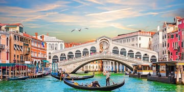 a group of people in a boat on a canal with Rialto Bridge in the background