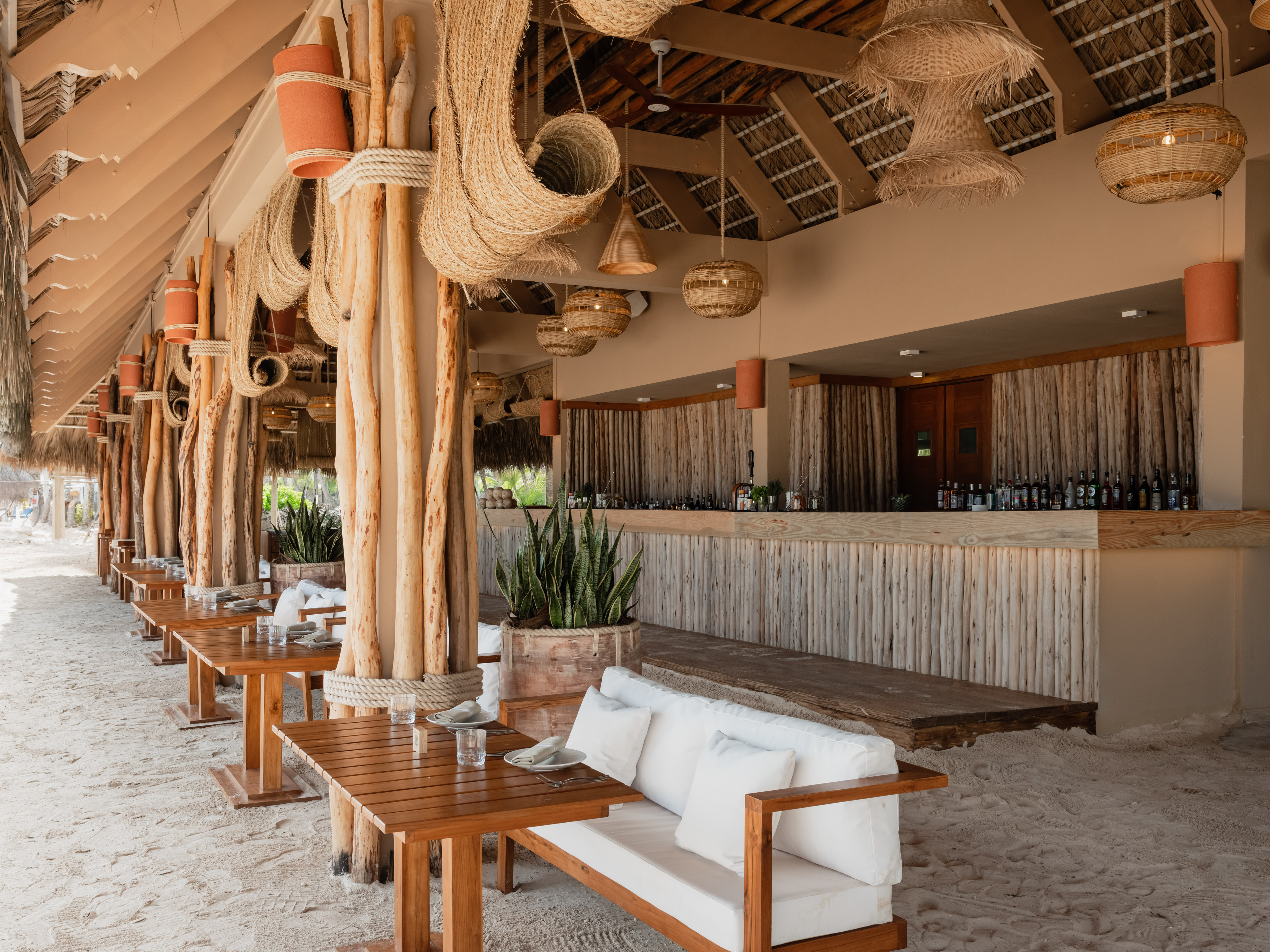Bohemian beach restaurant with sand floor, wood tables, and straw decor.