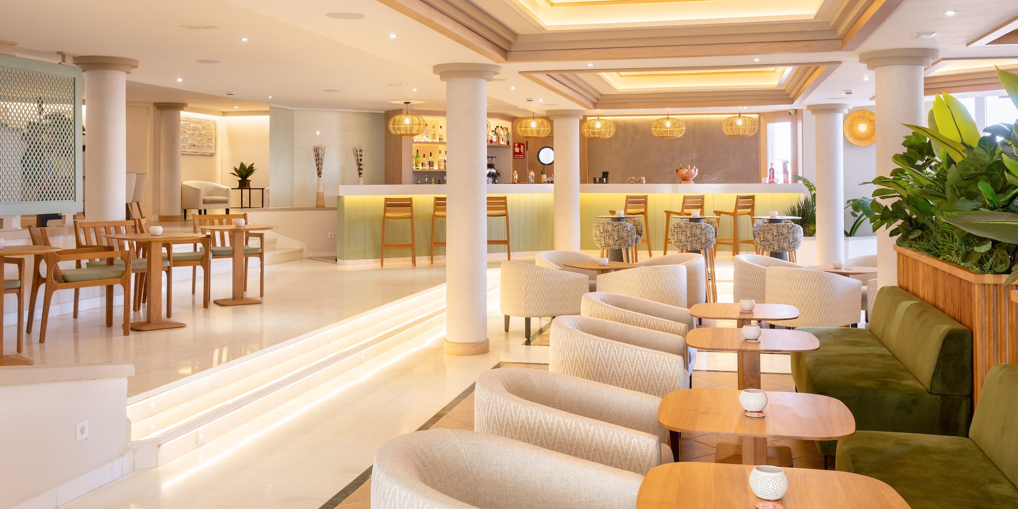 Modern hotel bar lounge with light wood, cream armchairs, and warm lighting.