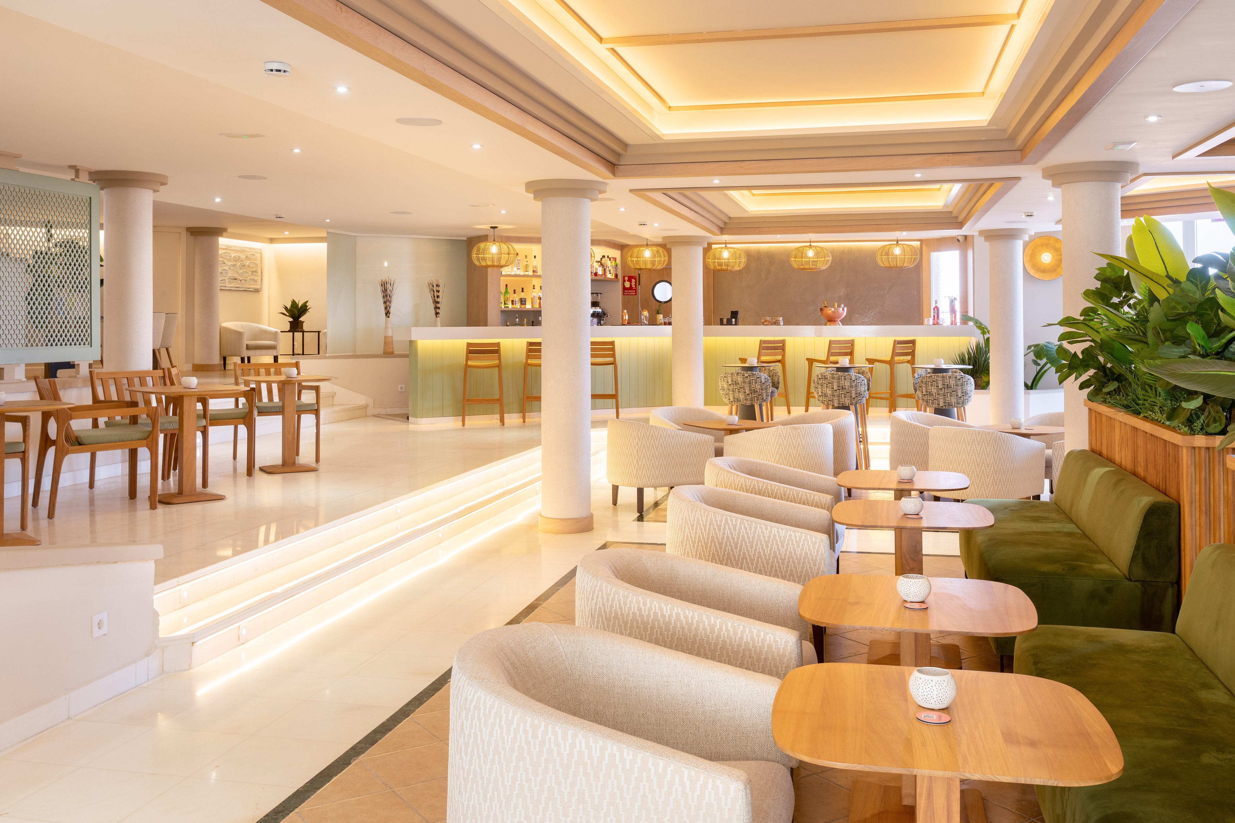 Modern hotel bar lounge with light wood, cream armchairs, and warm lighting.