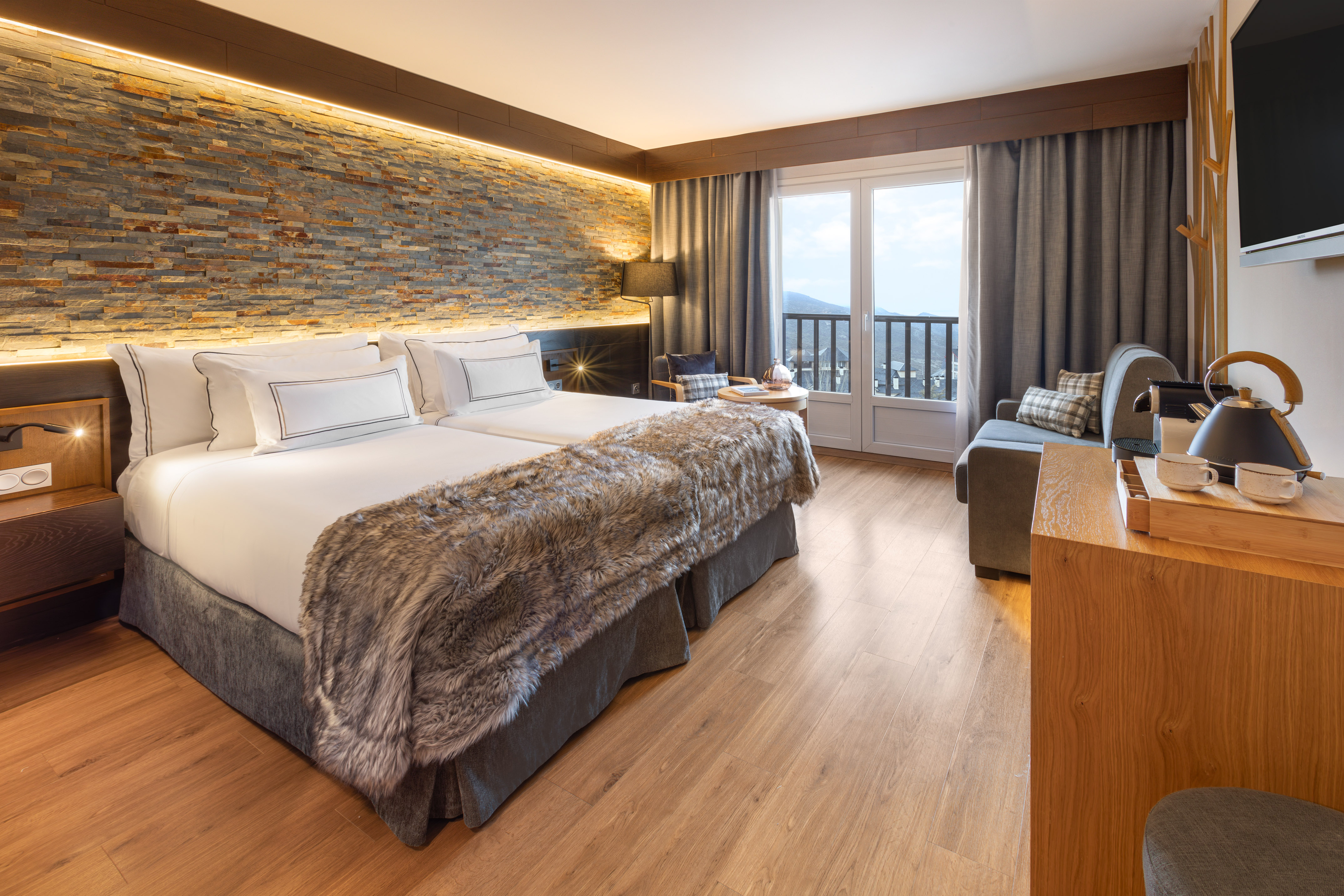Cozy hotel room with twin beds, stone wall, fur blanket, mountain view.