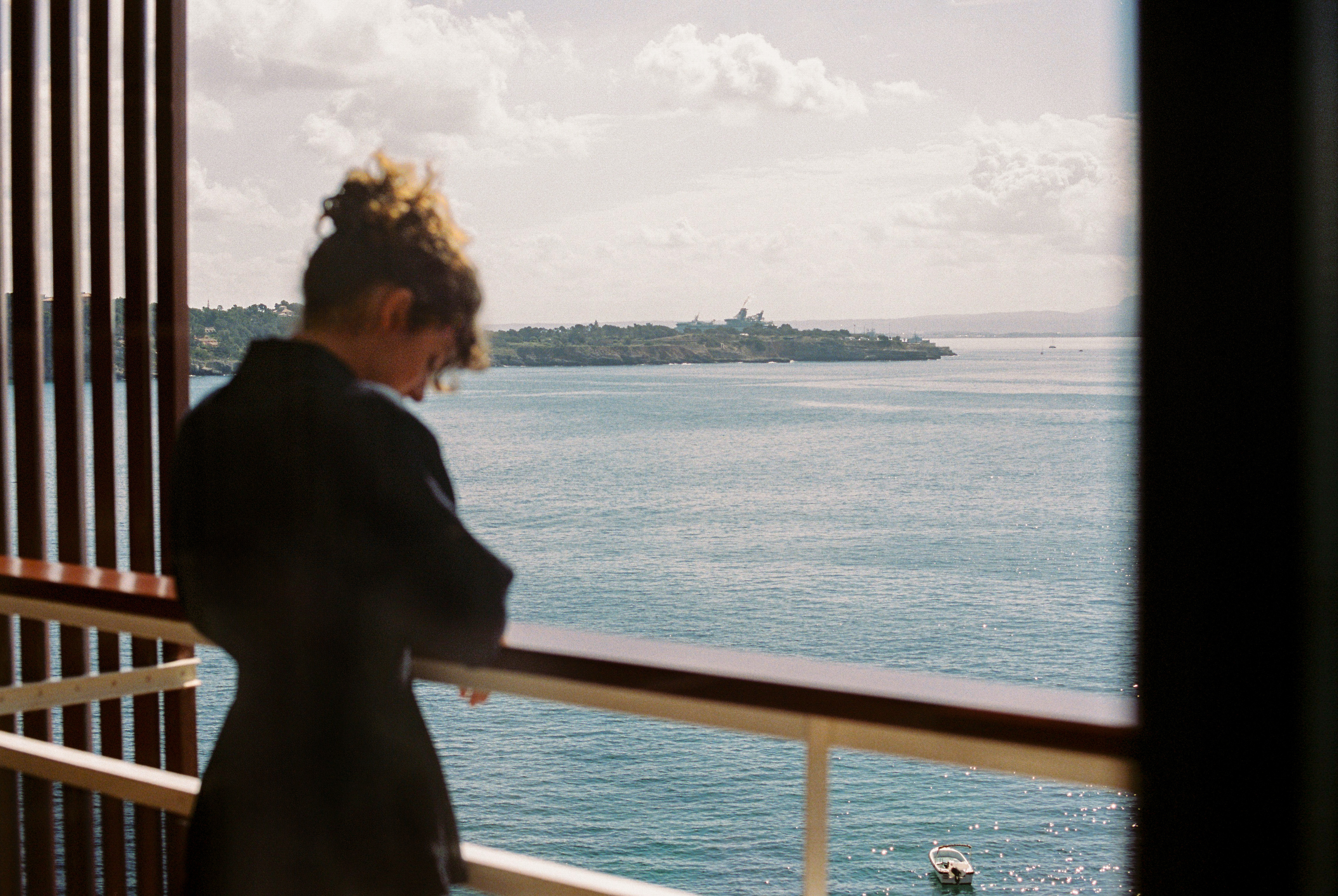 Mujer en balcón con vista al mar, paisaje costero y bote.