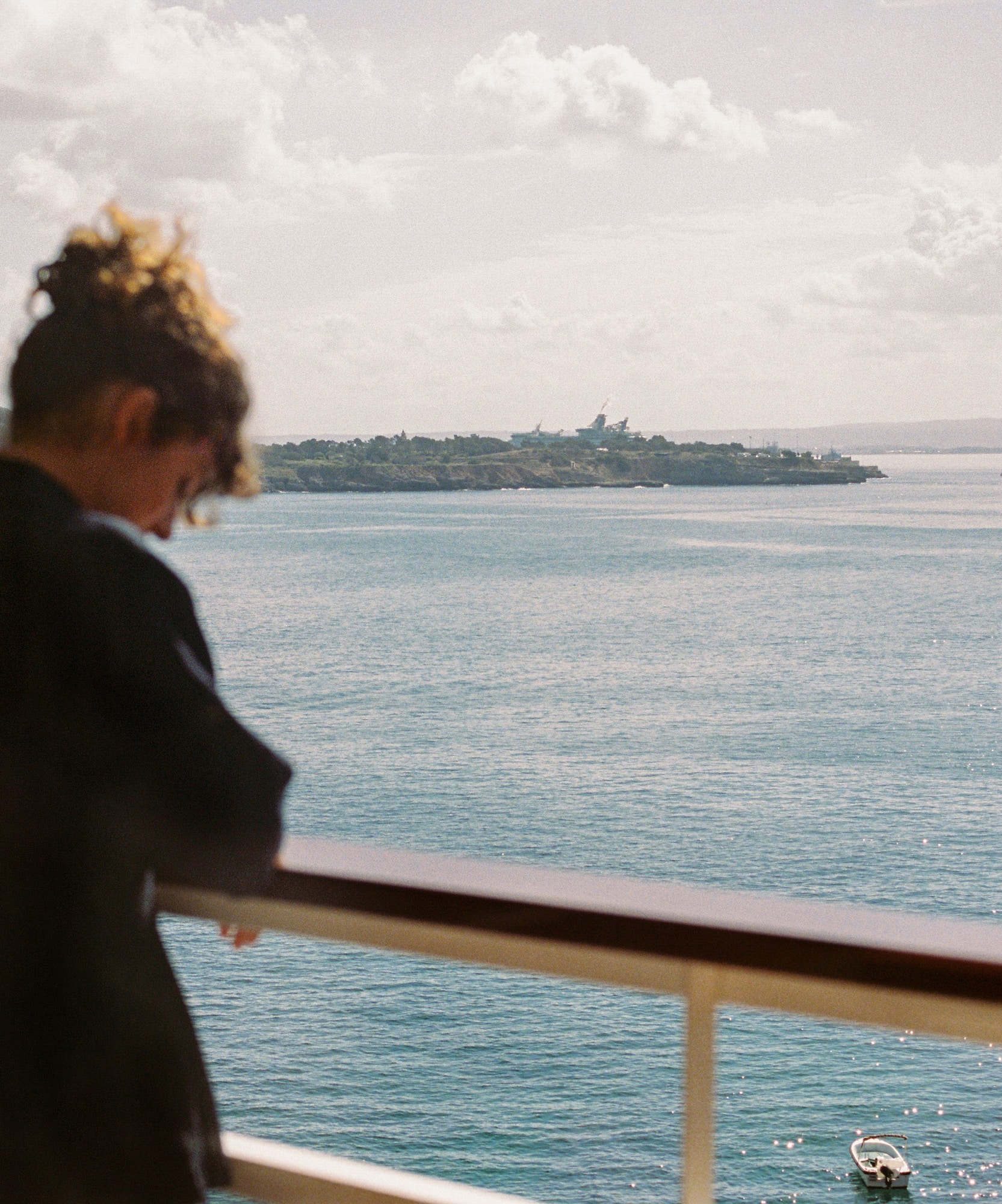 Mujer en balcón con vista al mar, paisaje costero y bote.