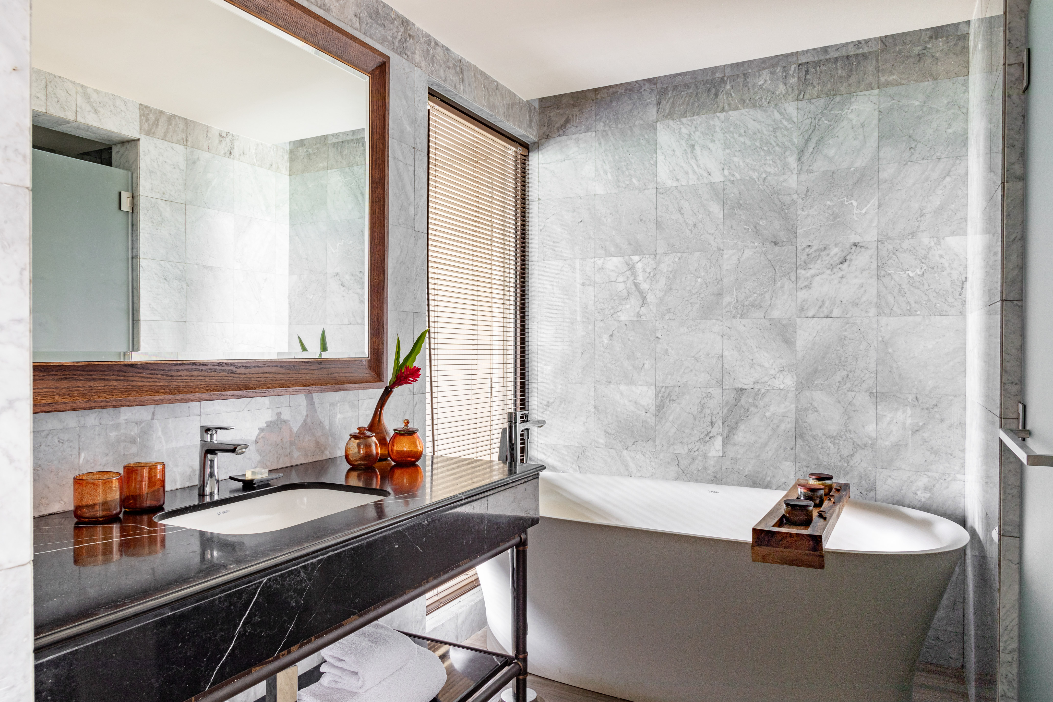 Luxury bathroom with grey marble walls, black vanity, and white freestanding bathtub.