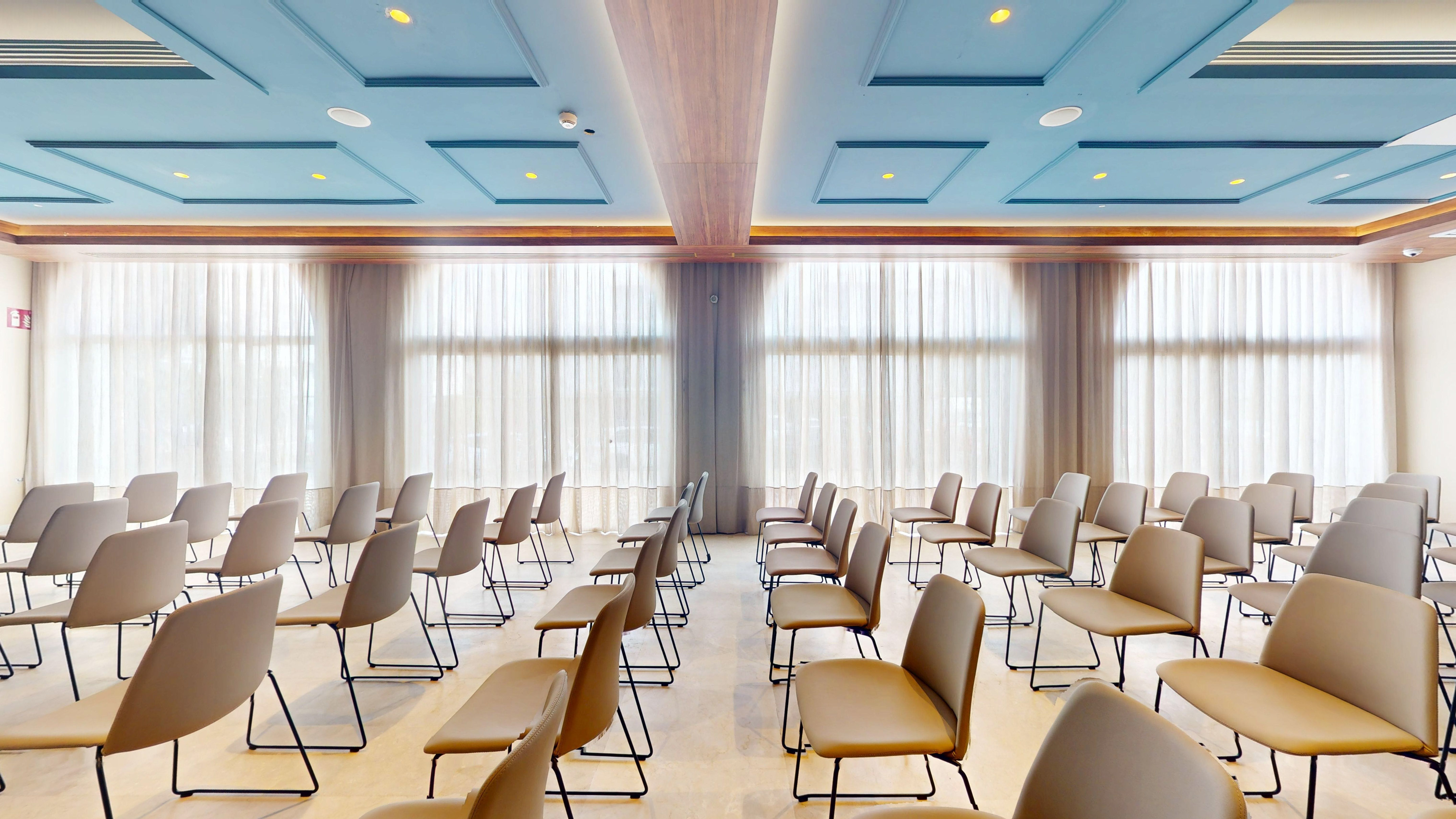 Empty modern conference room with rows of chairs and large windows.