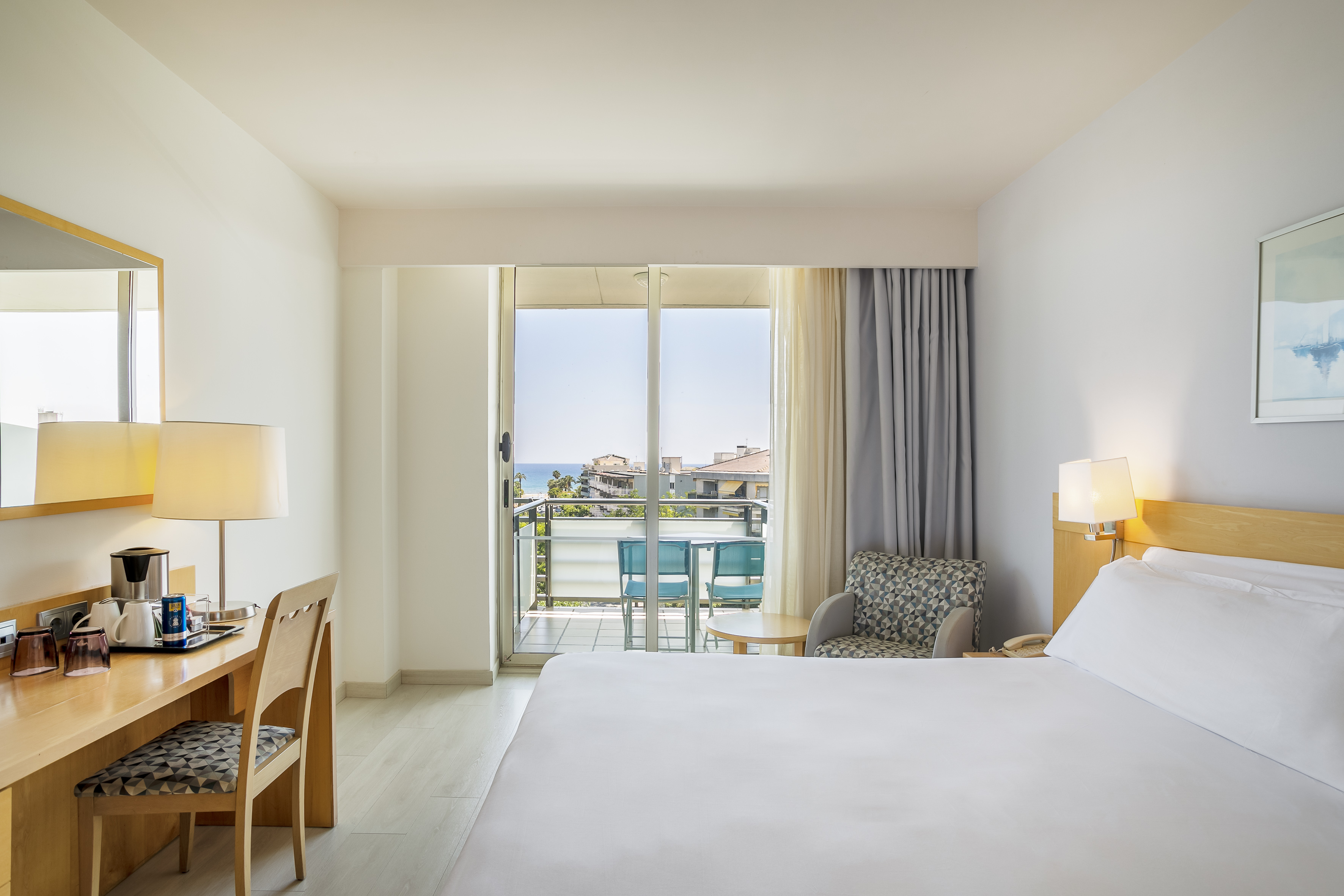 Hotel bedroom with balcony, ocean view, desk, and armchair.