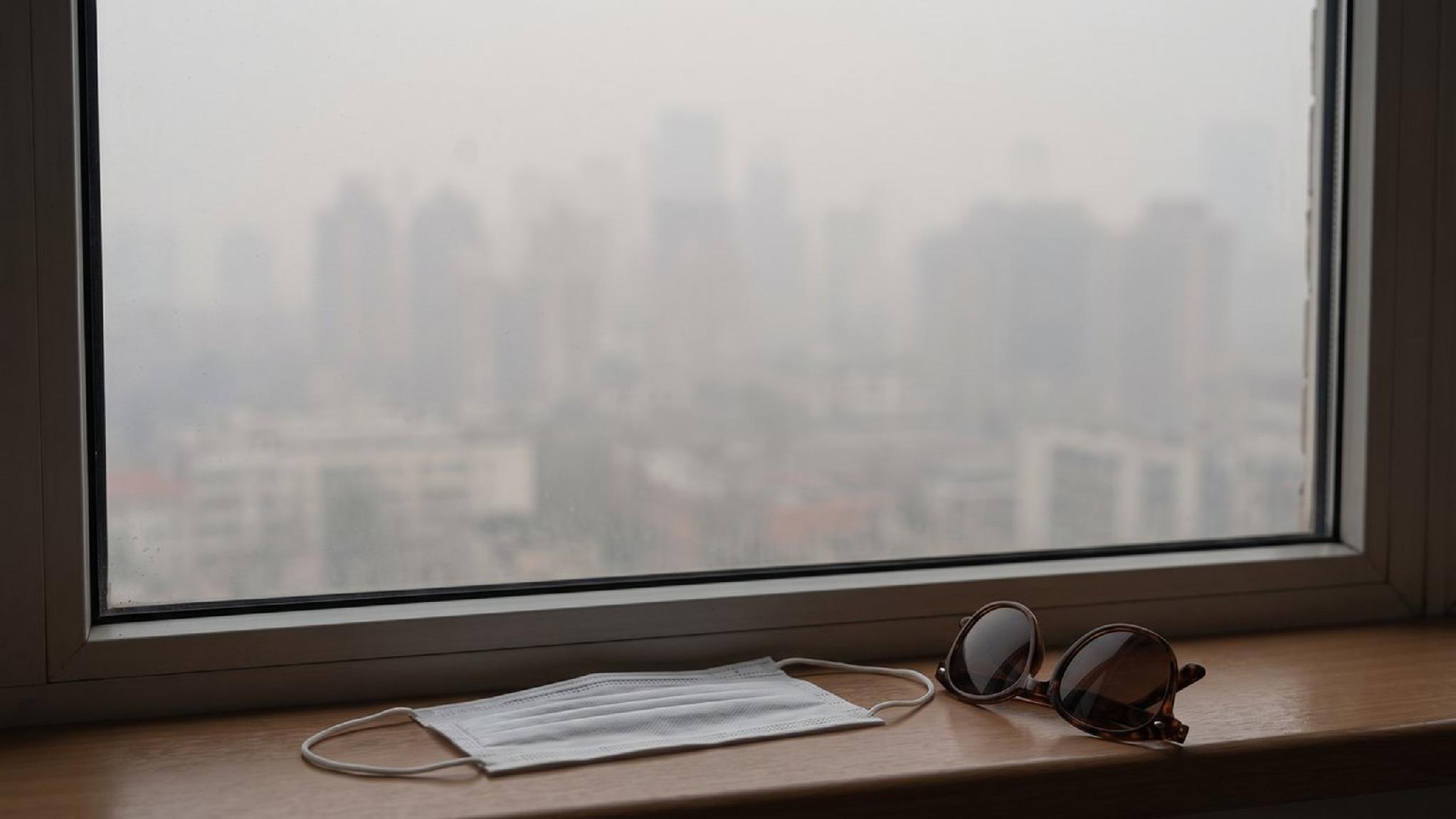 Mask and sunglasses on window sill, city view hazy from air pollution.