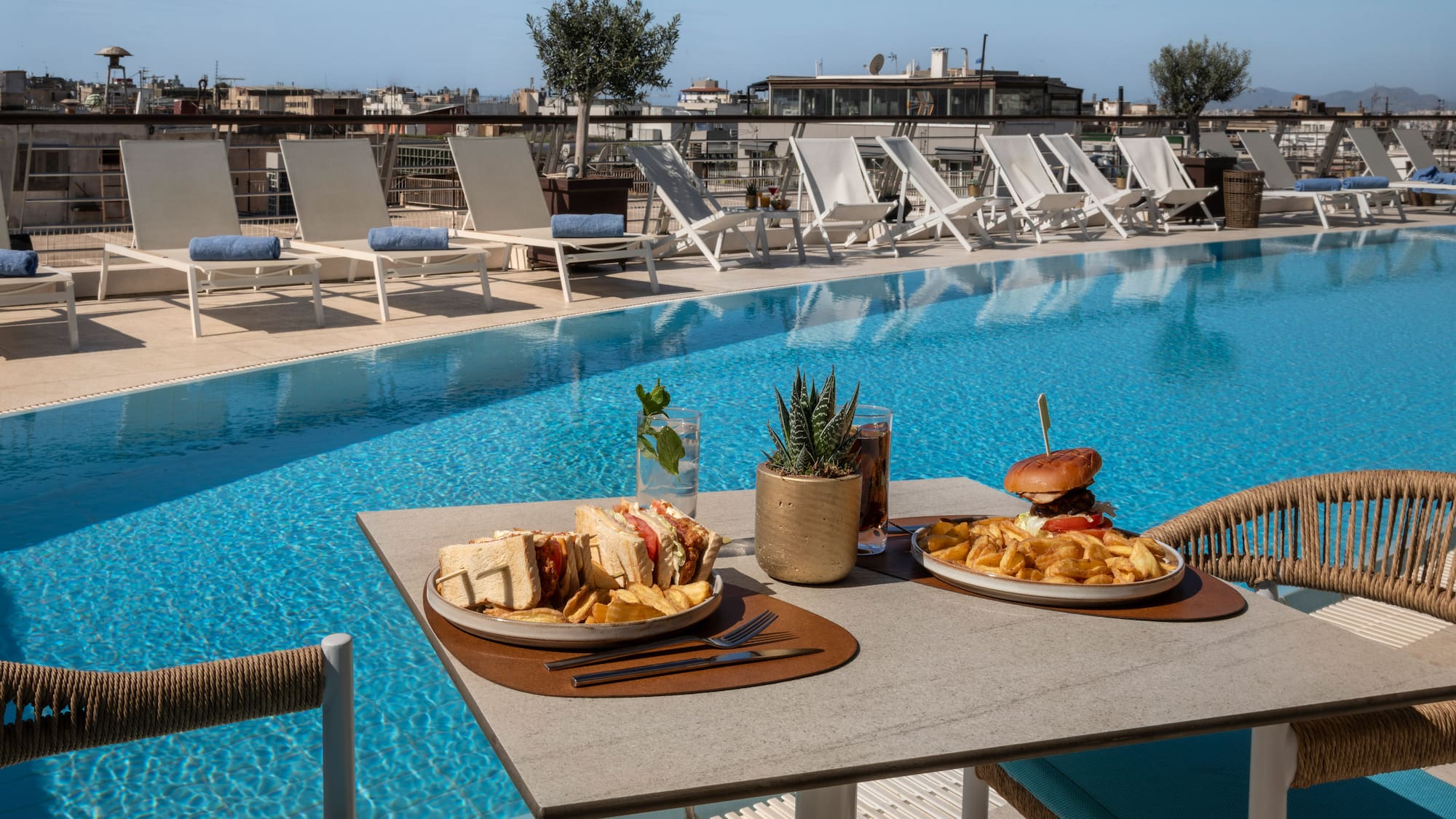 Luxury hotel rooftop pool lunch with burger, club sandwich, and fries.