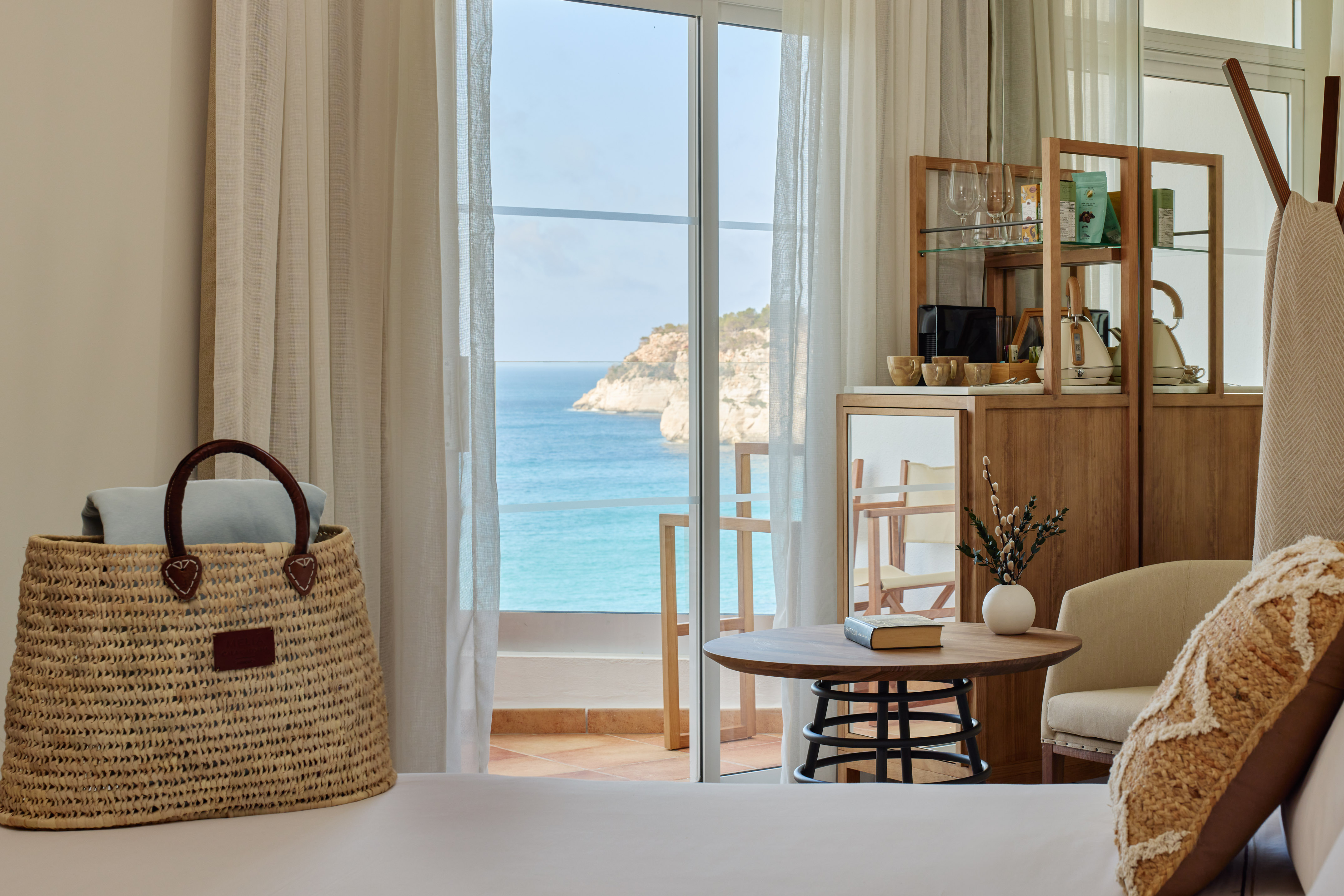 Coastal hotel room with a balcony overlooking the turquoise sea and cliffs.