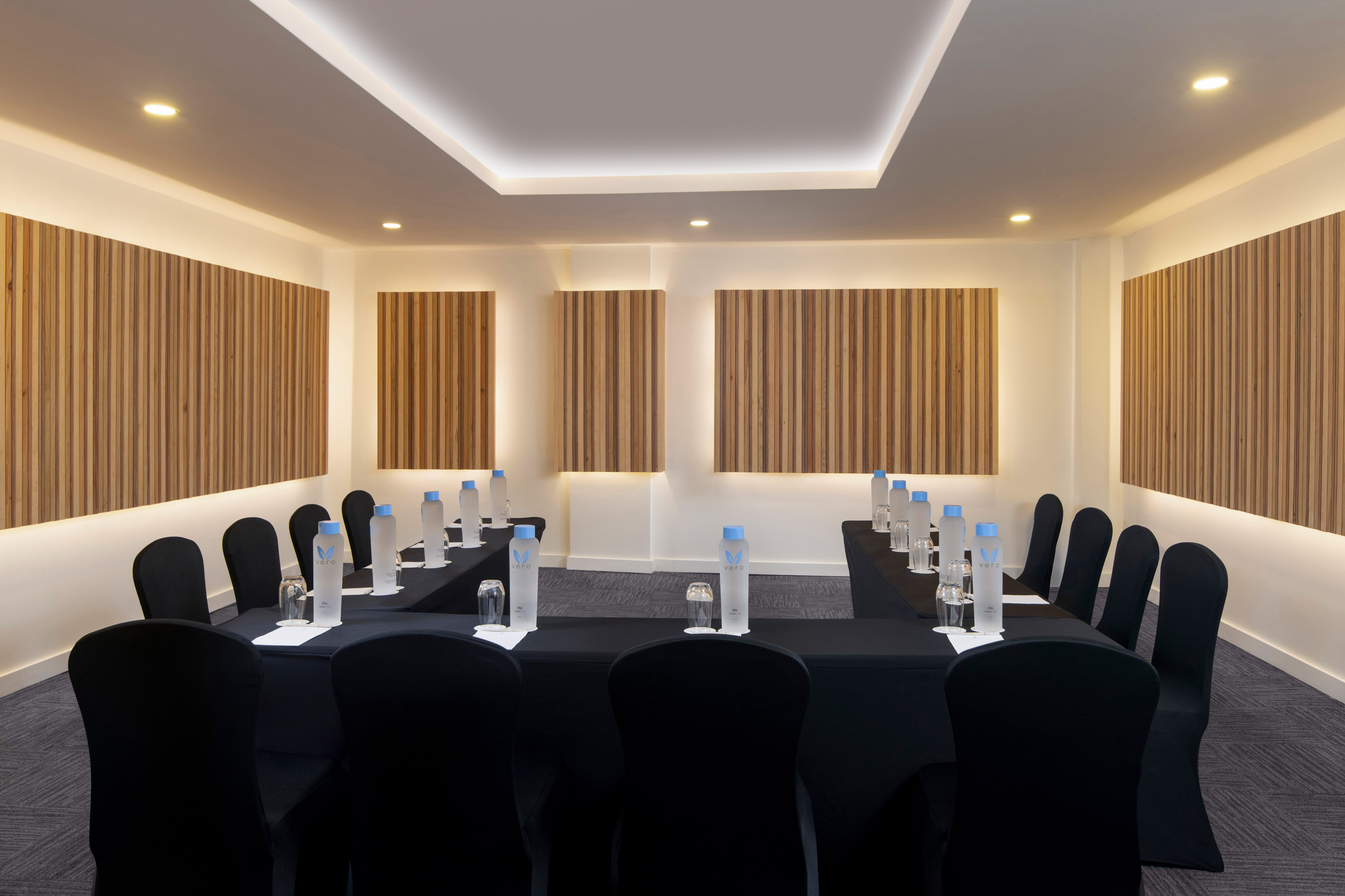 Modern conference room with U-shaped table setup, black chairs, and wood slat walls.