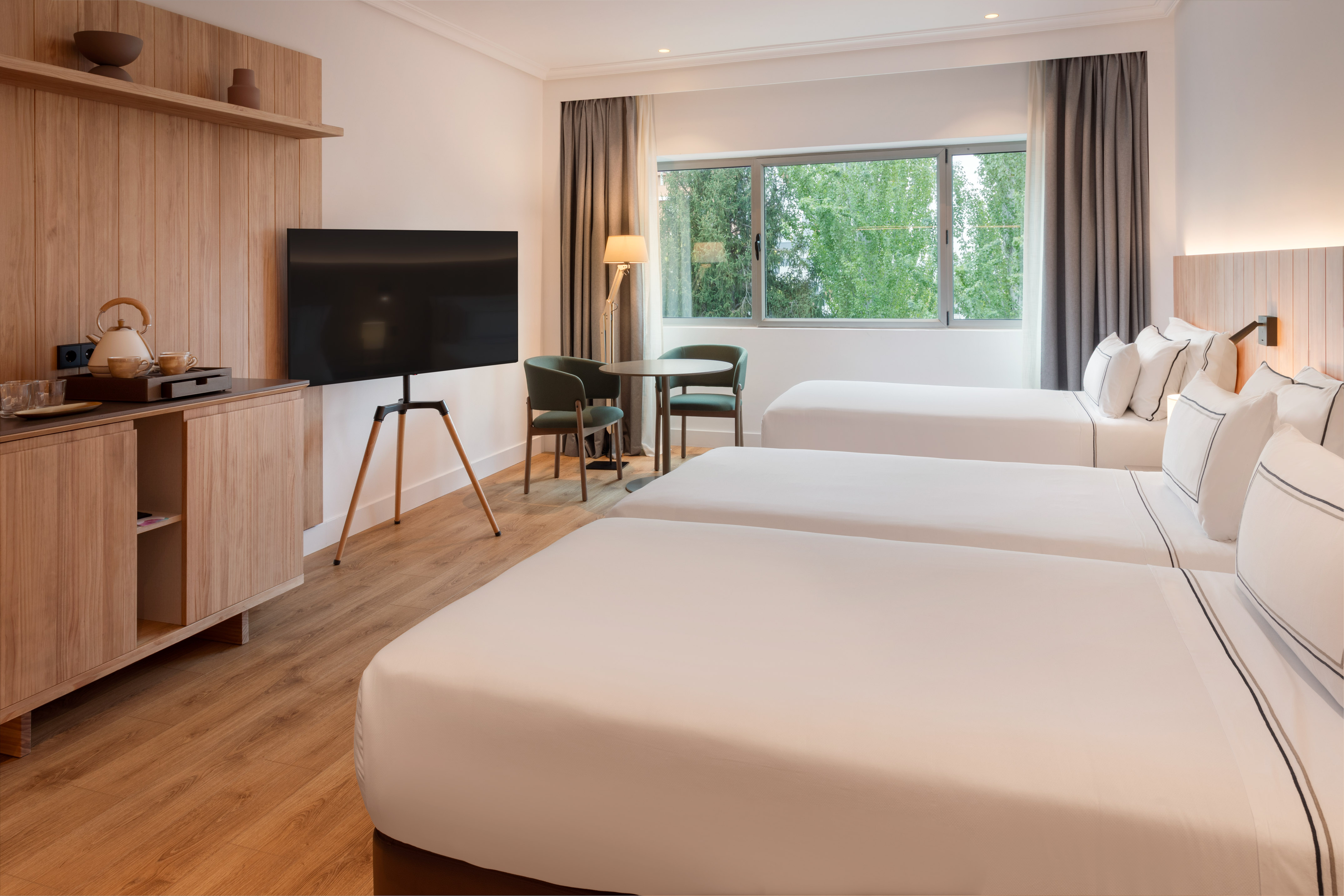 Modern triple hotel room with three single beds, wood decor, TV, and large window.