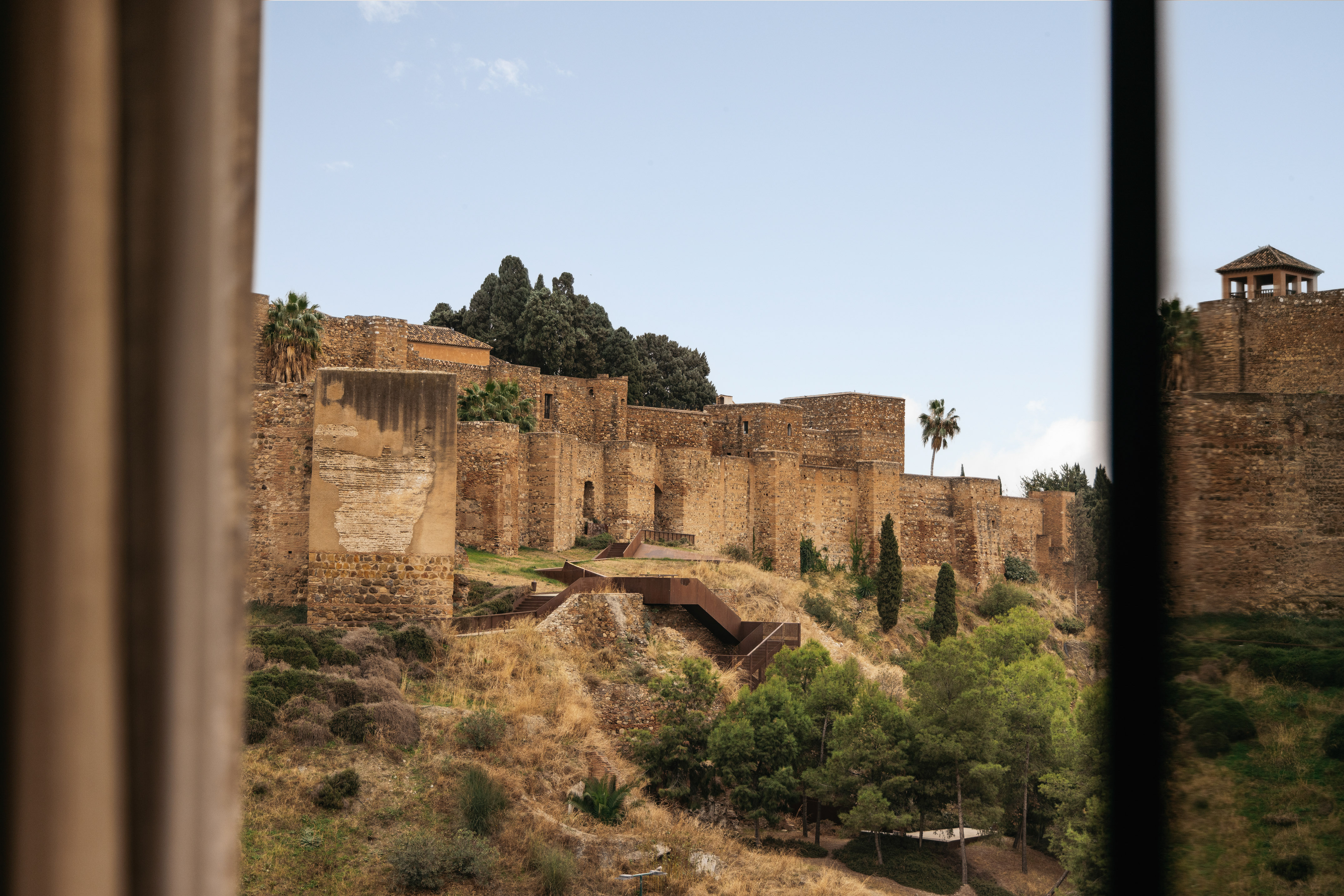 Alcazaba of Malaga stone fortress walls, hillside, palm trees, and pathways.