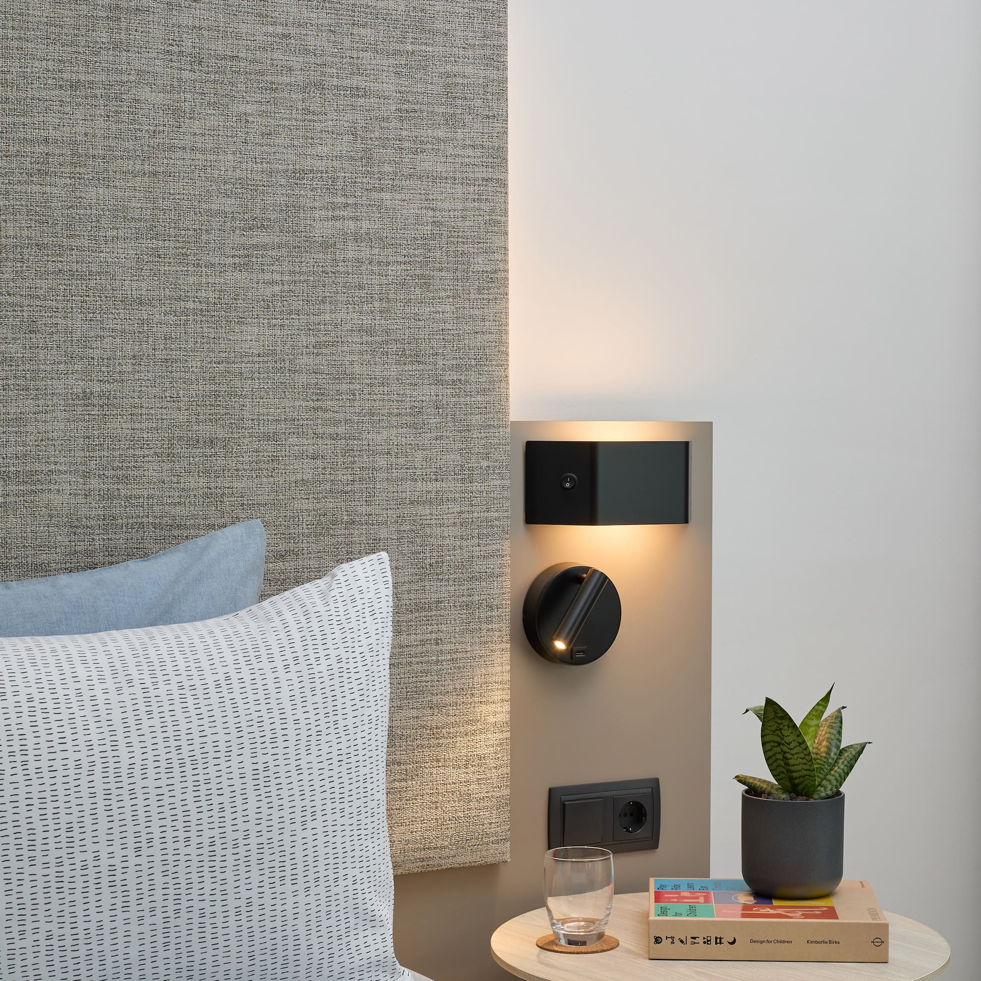 a small table with a plant on it next to a bed