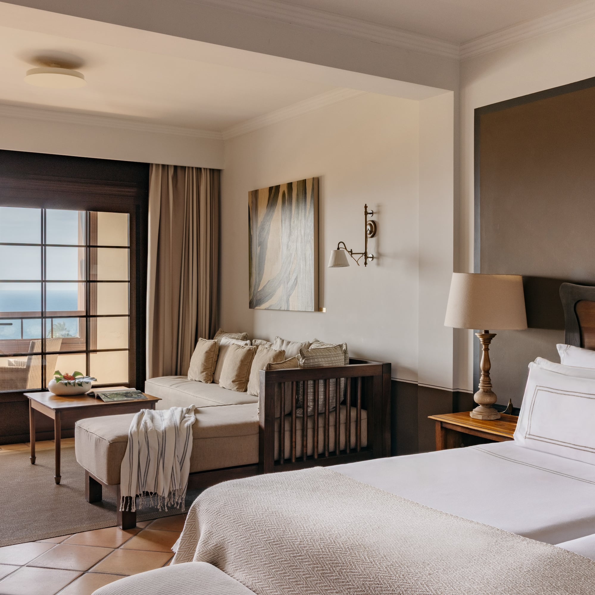 Hotel suite with ocean view balcony, two beds, sofa, and living space.