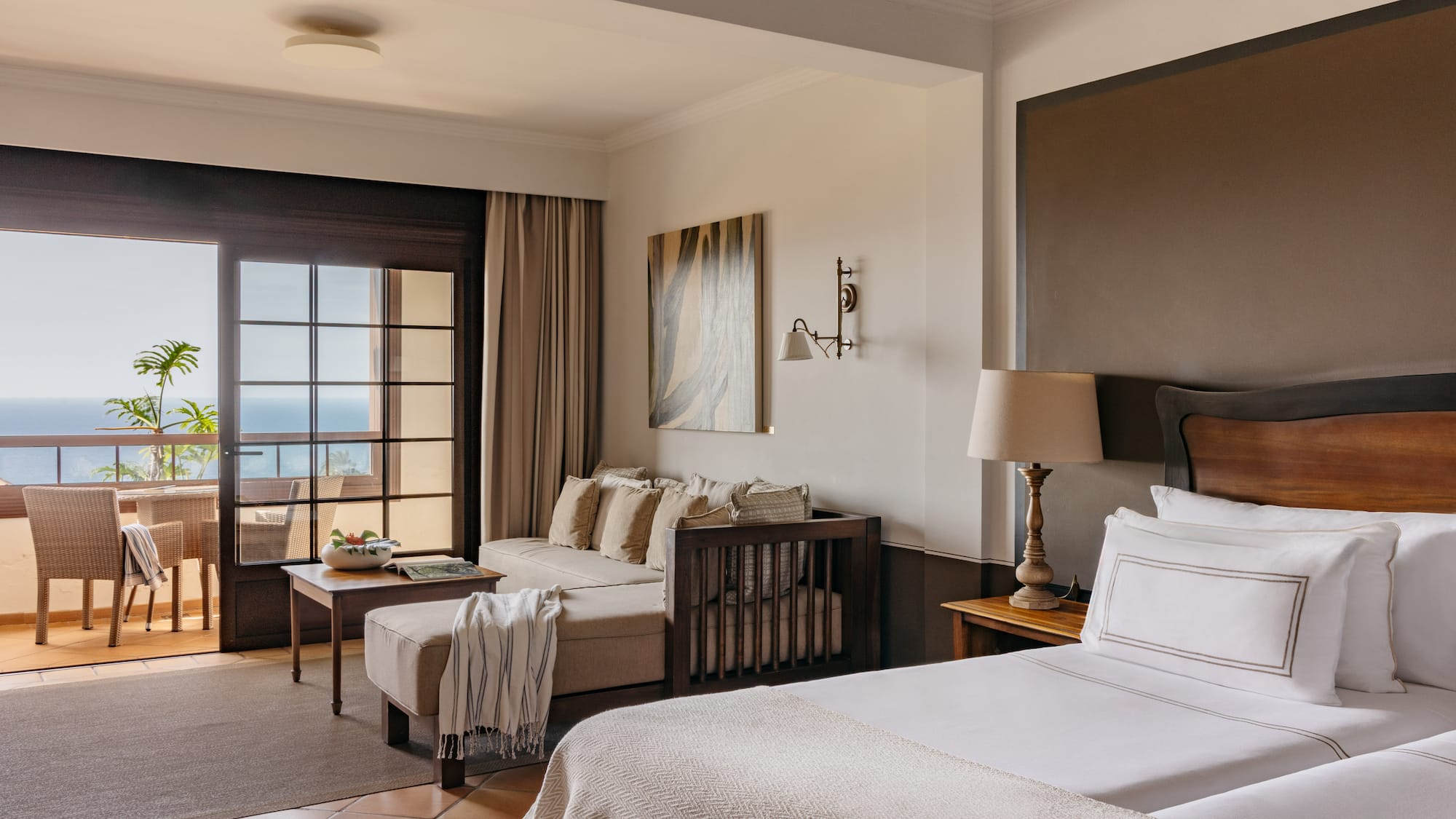 Hotel suite with ocean view balcony, two beds, sofa, and living space.