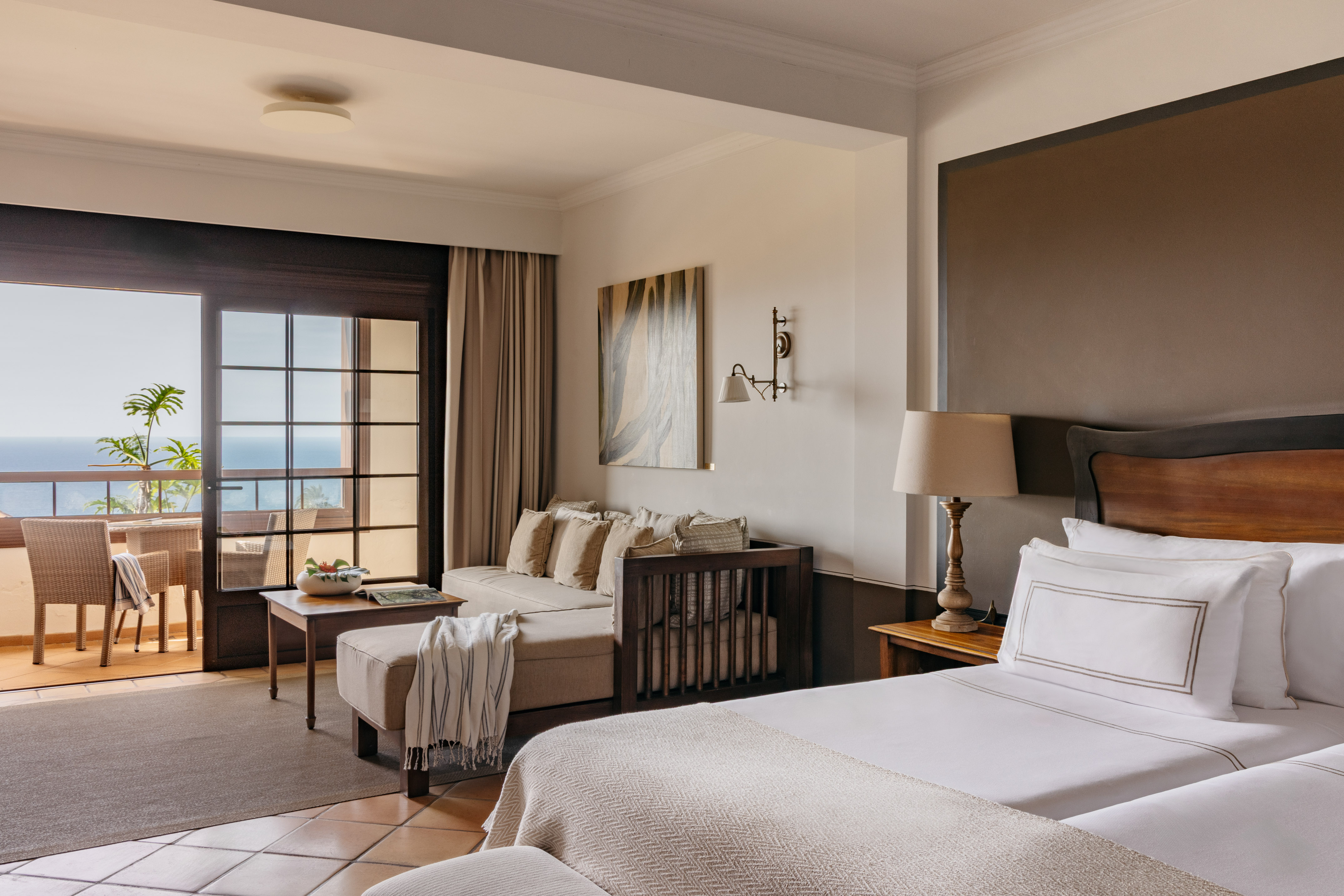 Hotel suite with ocean view balcony, two beds, sofa, and living space.